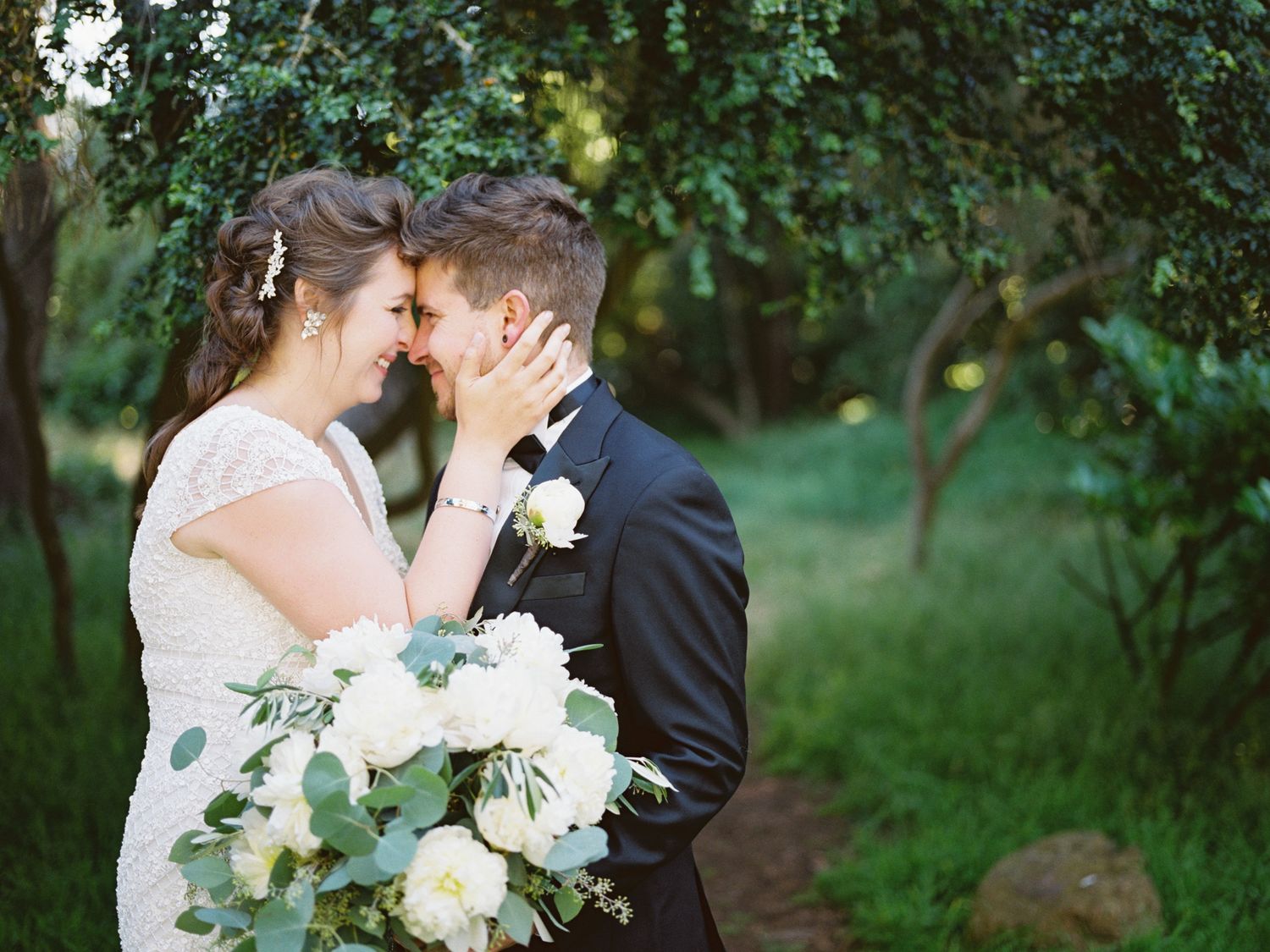 A romantic wedding moment in a lush garden setting with white flowers and greenery as the couple shares an intimate embrace.