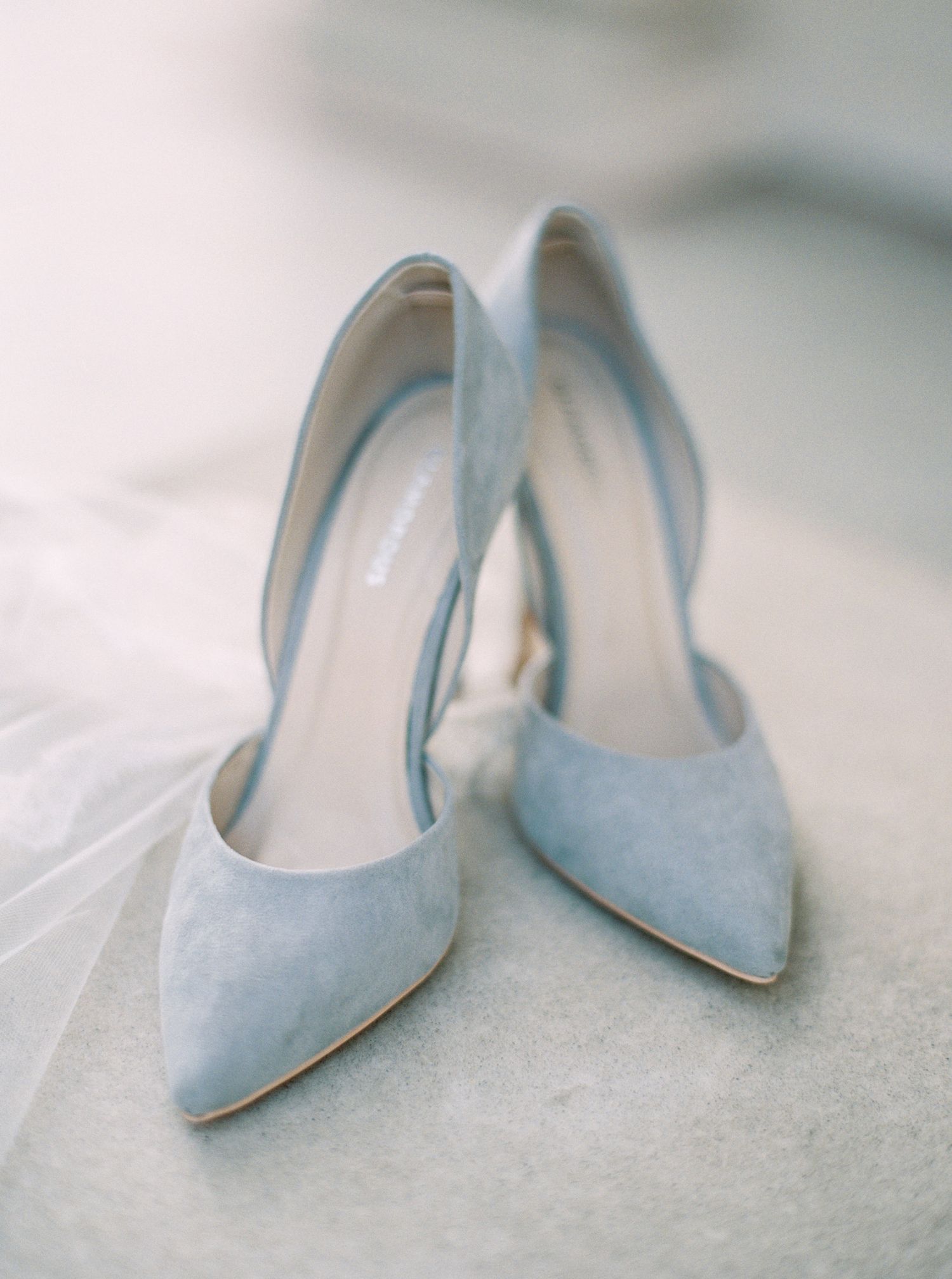 Elegant light blue suede stiletto heels arranged in a row on a textured white surface.