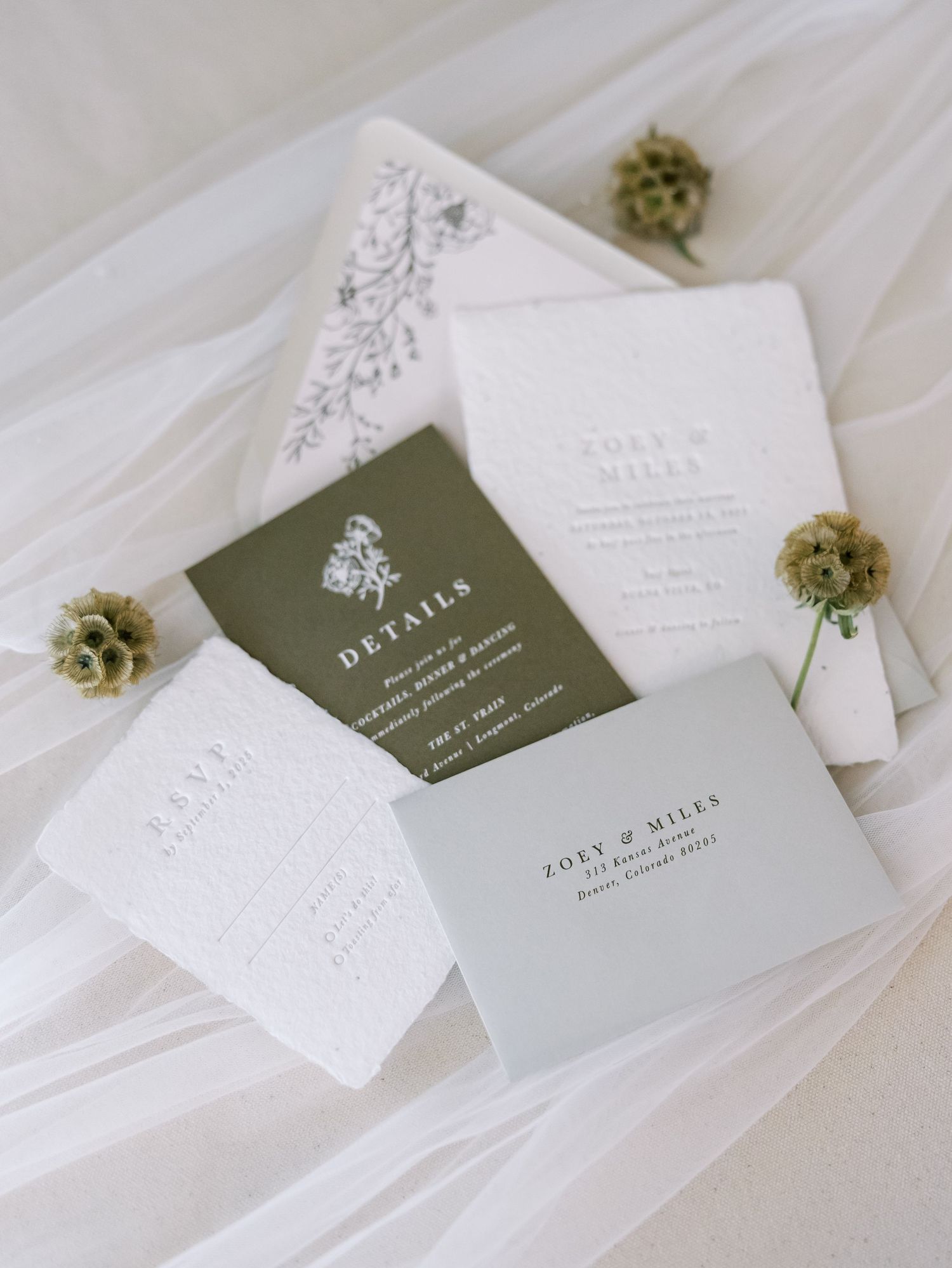 Elegant wedding invitation suite with olive green details card, white embossed stationery, floral envelope liner, and addressed envelope.