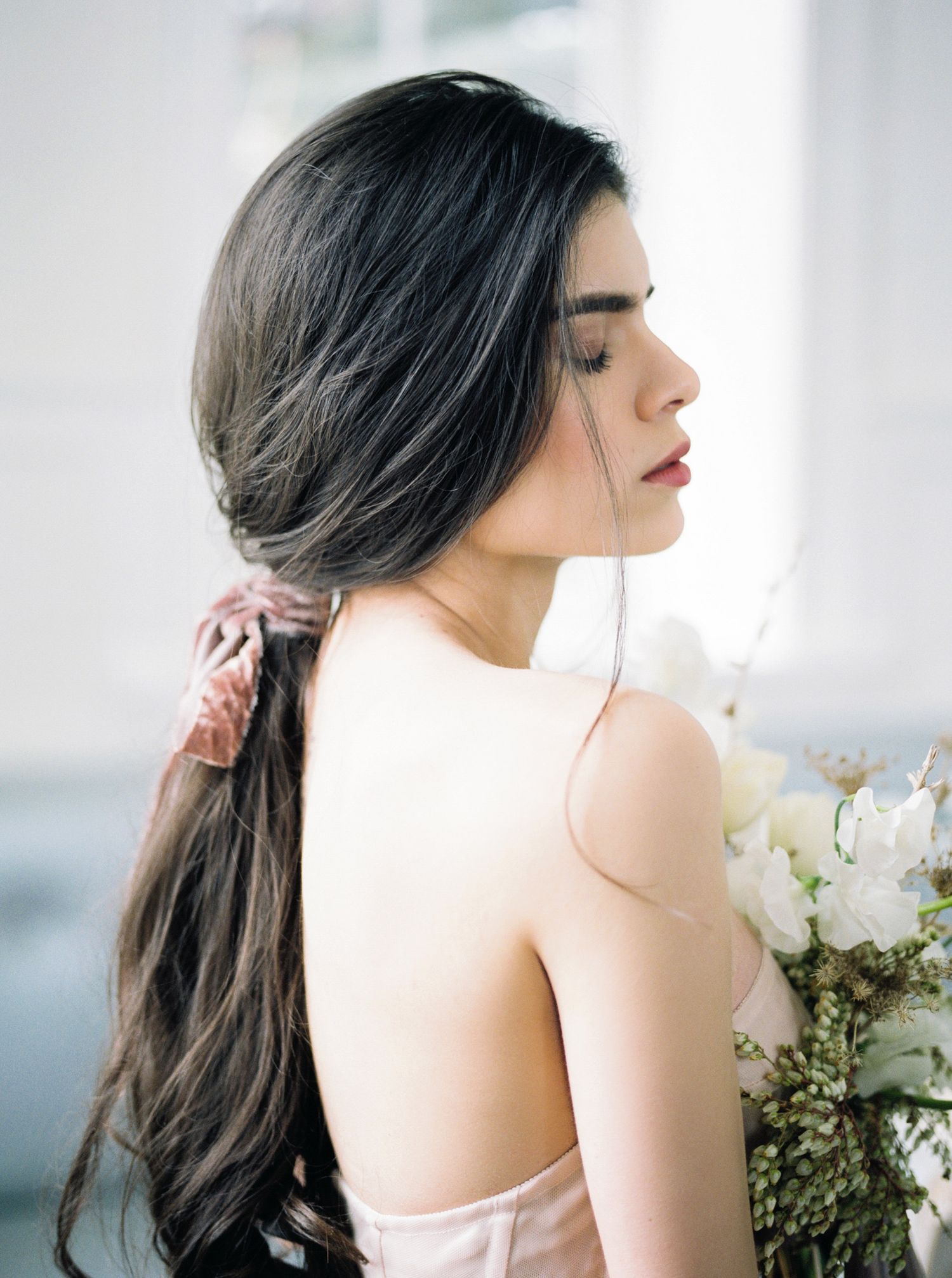 Romantic side profile shots of a bride with flowing dark hair wearing a light gown against a bright window backdrop.