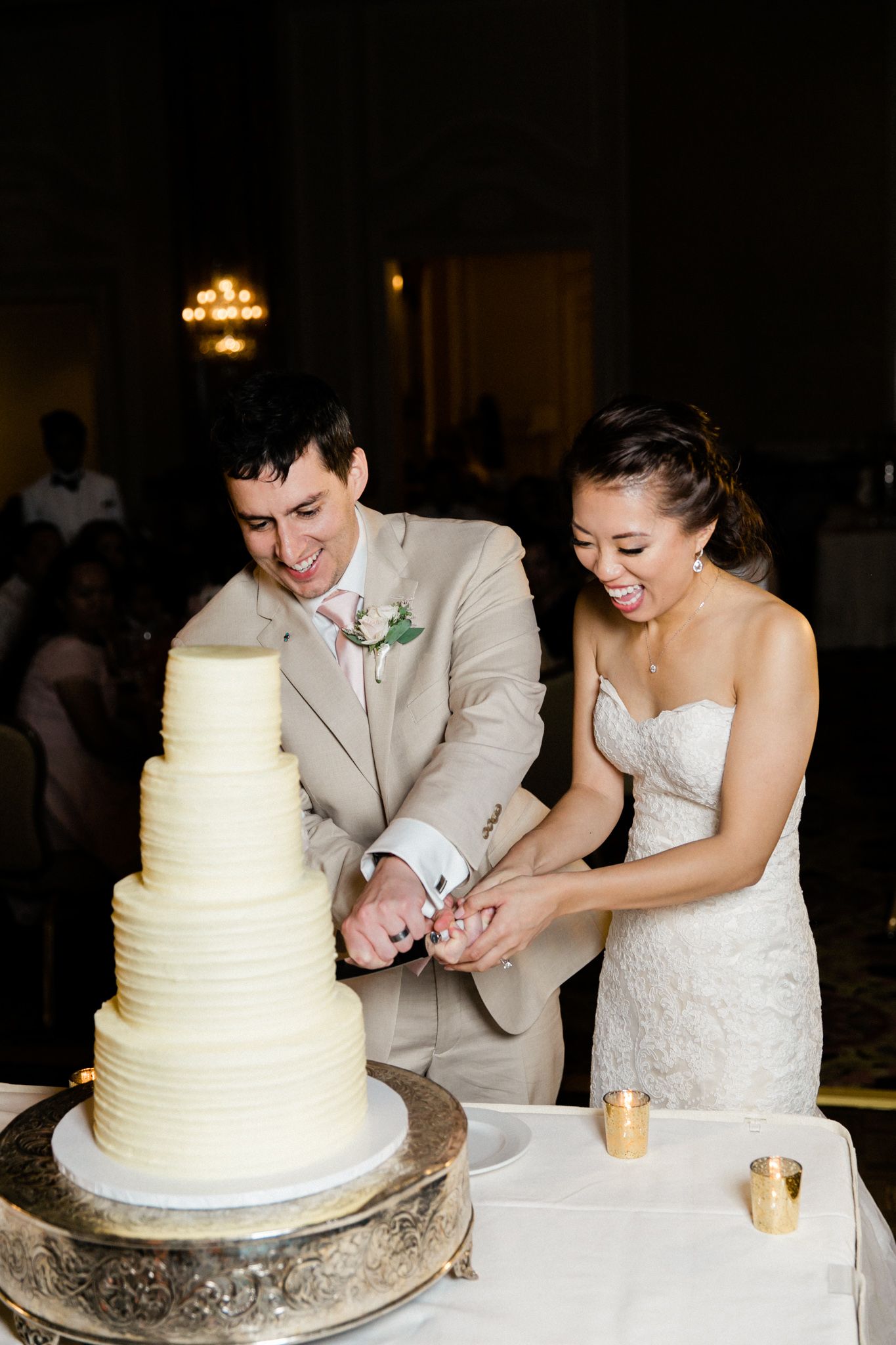 A joyful wedding couple cutting their elegant white tiered cake together at their reception.