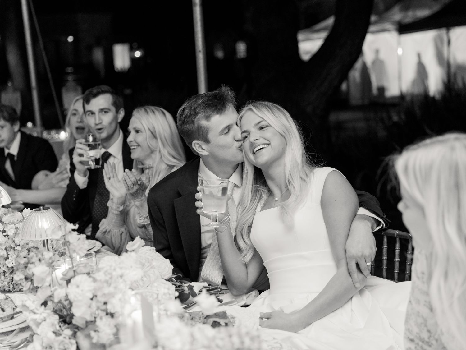 Black and white candid reception photos showing guests laughing and celebrating at dining tables.