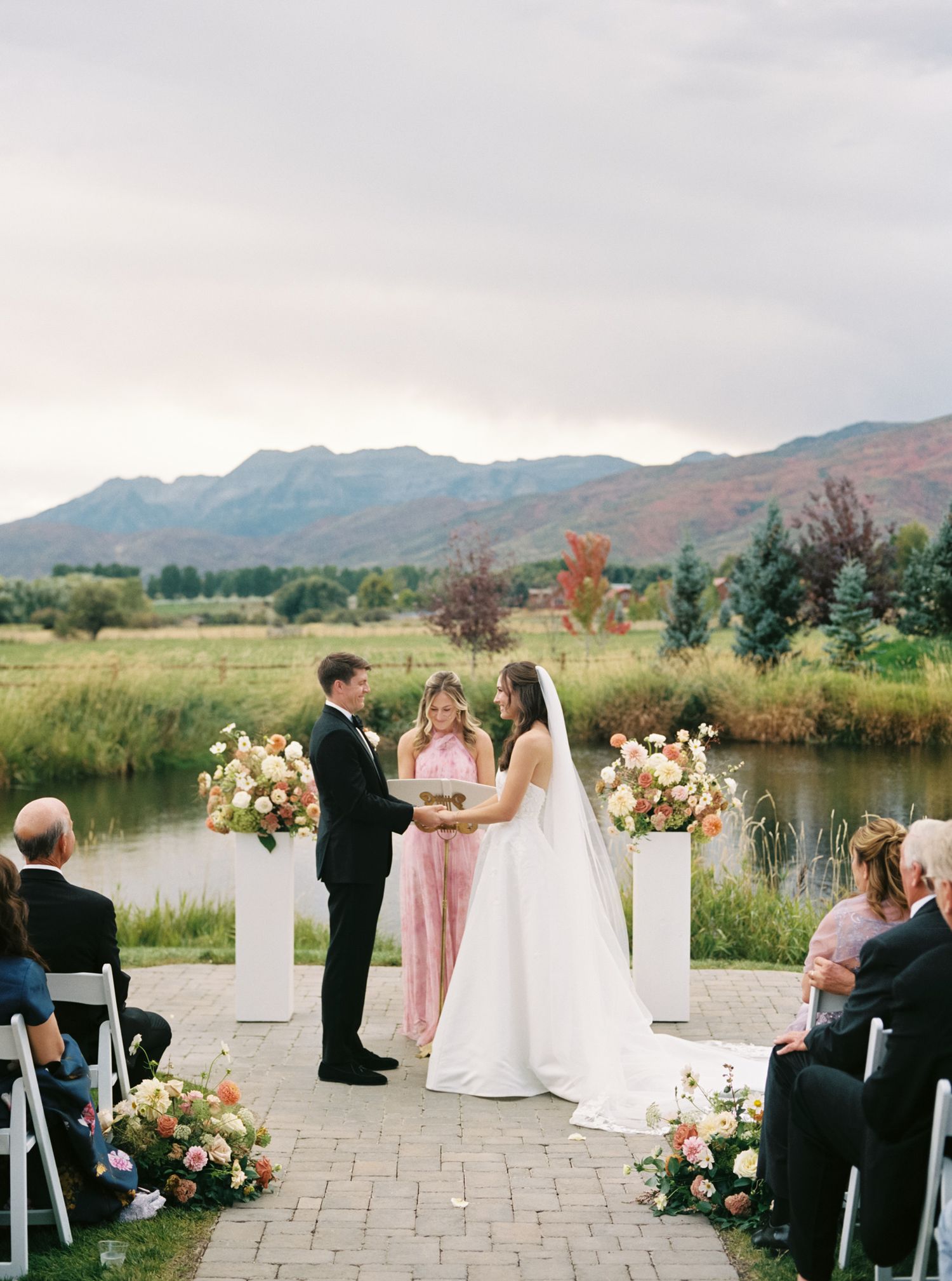 Wedding ceremony setup outdoors with floral arrangements and white chairs against a mountain backdrop.