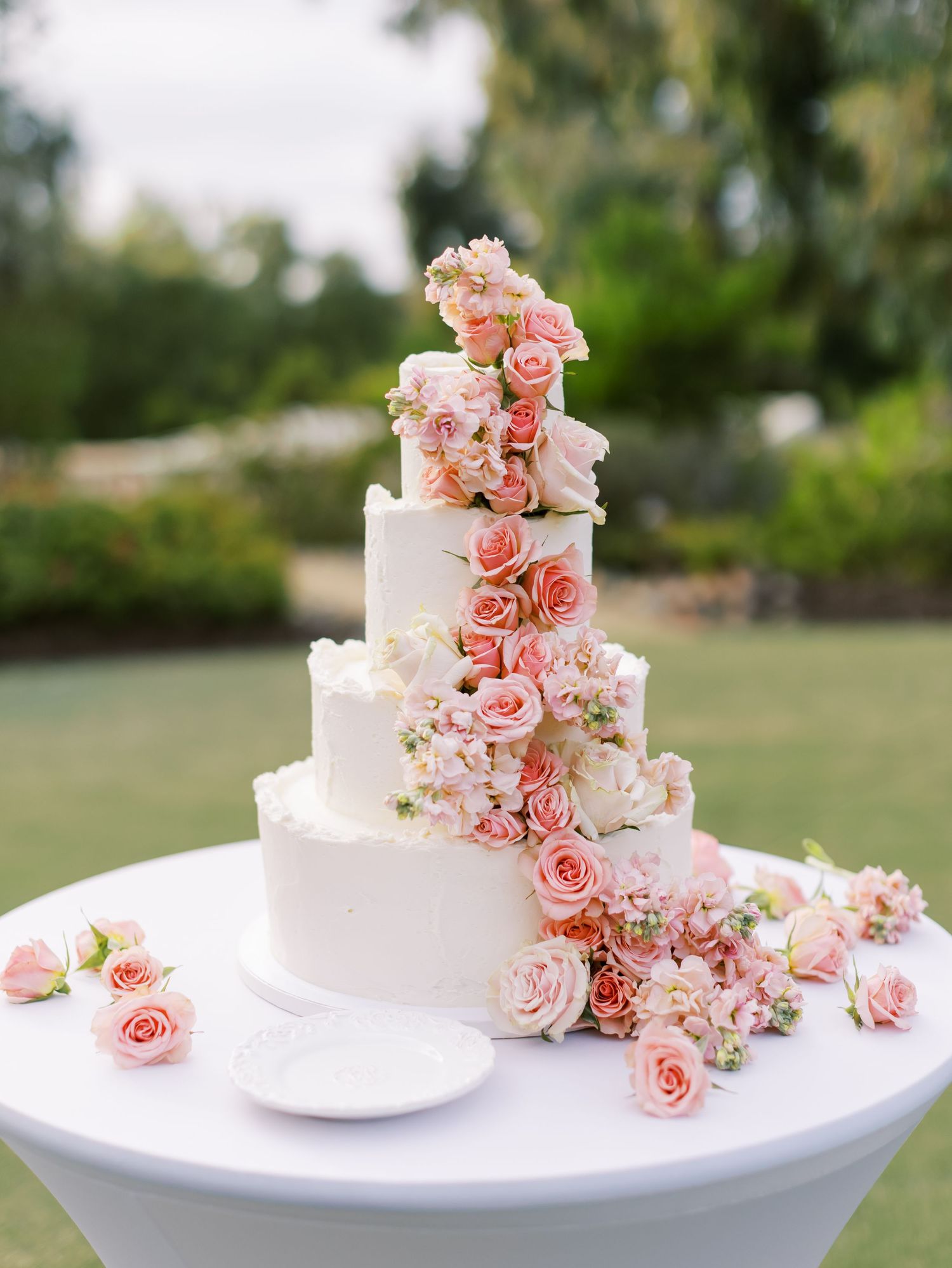 Elegant white wedding cake decorated with cascading pink roses and flowers on a white stand.