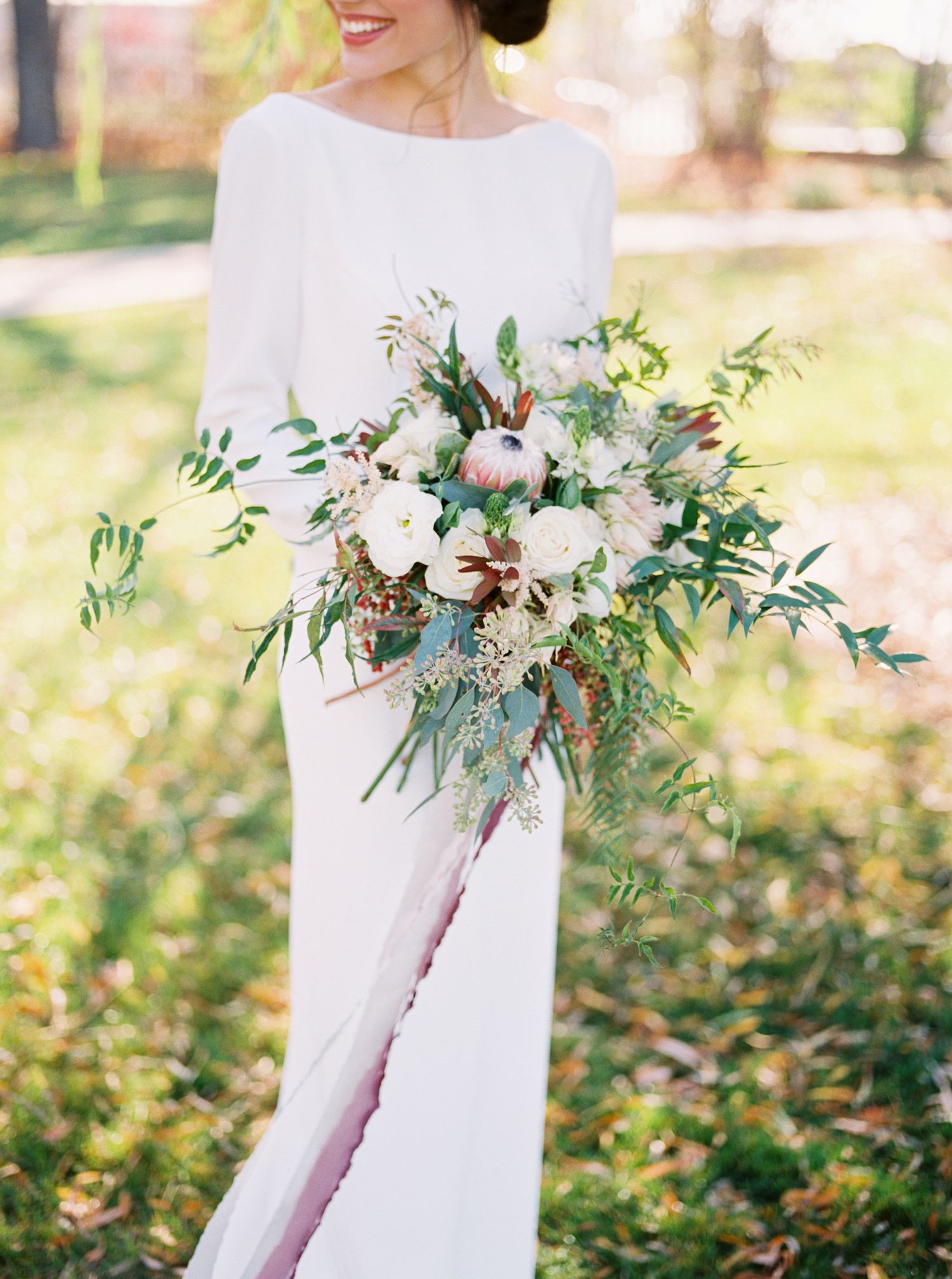 A delicate wedding bouquet featuring white flowers and green eucalyptus leaves against a simple white dress.