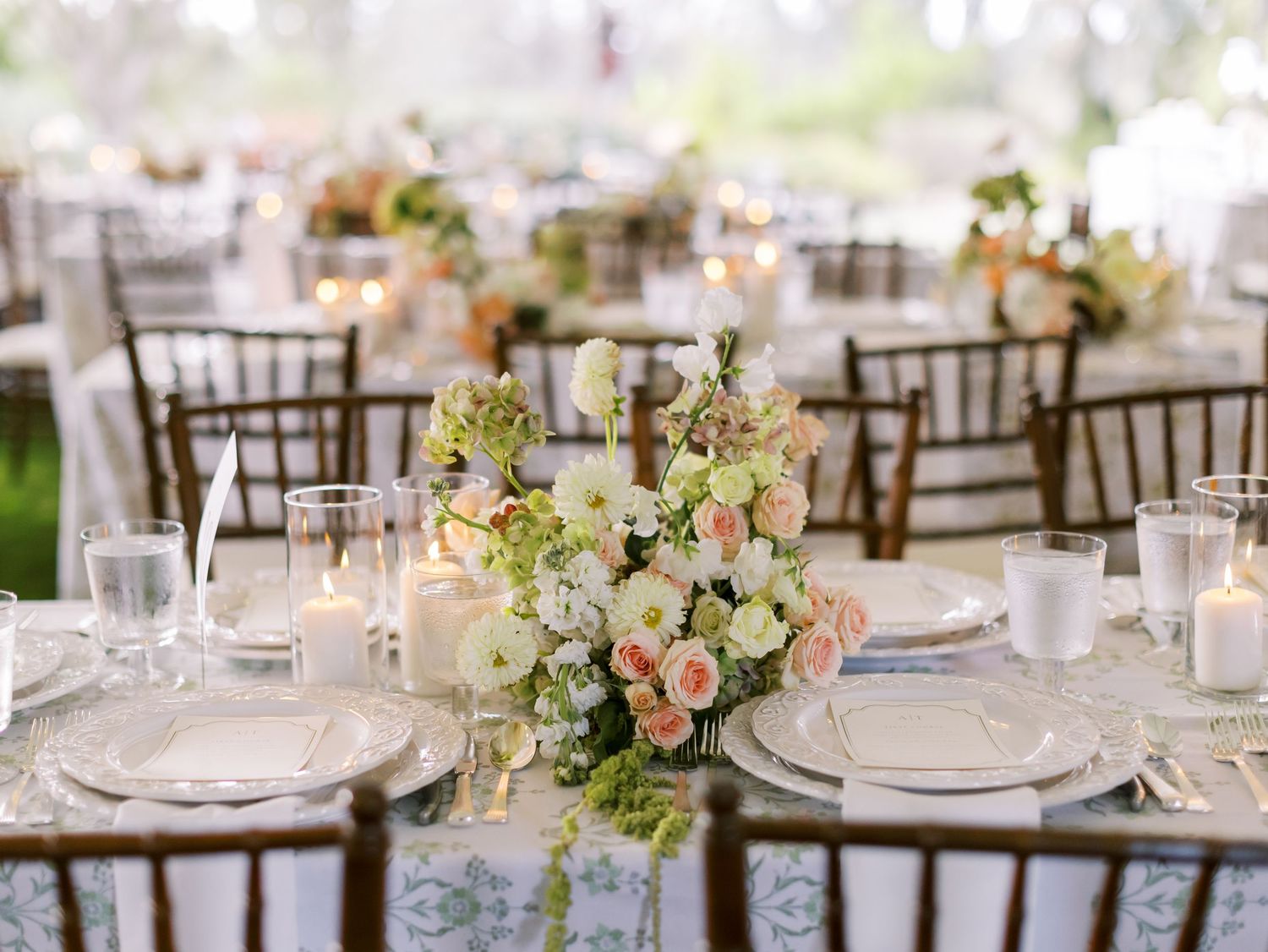 Wedding table decor featuring blush and white floral arrangements with dark chiavari chairs and lace linens.