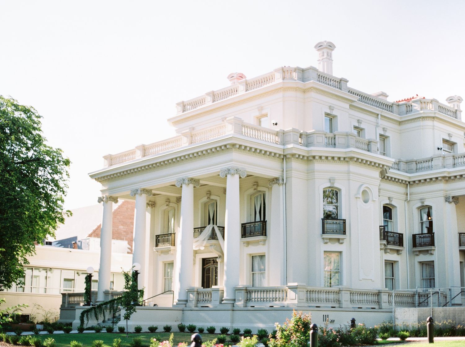 Panoramic view of a luxurious white mansion with classical architectural details and manicured gardens.