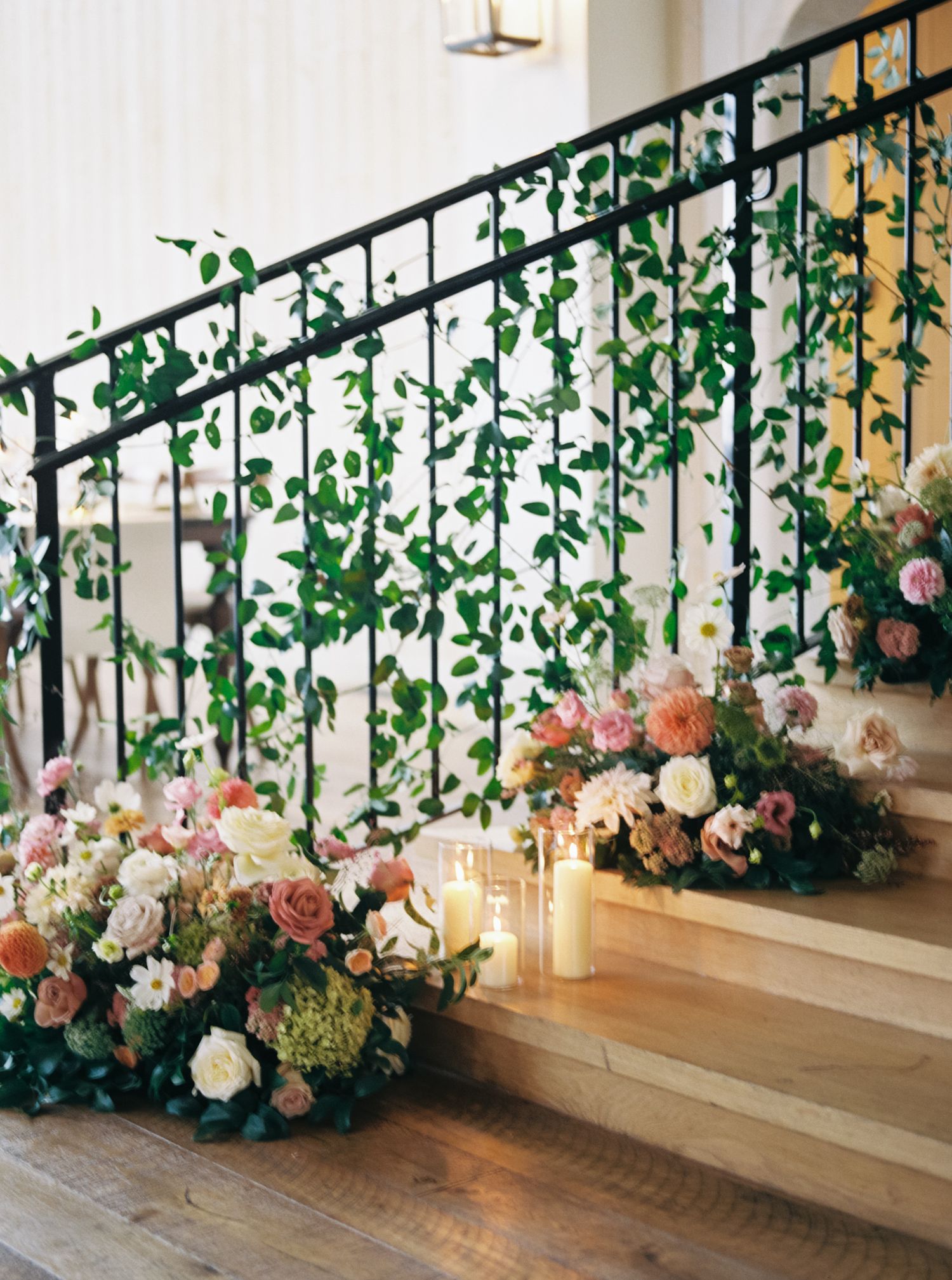 Elegant wedding decor featuring cascading greenery and pink roses along a wooden staircase with hanging glass orbs.