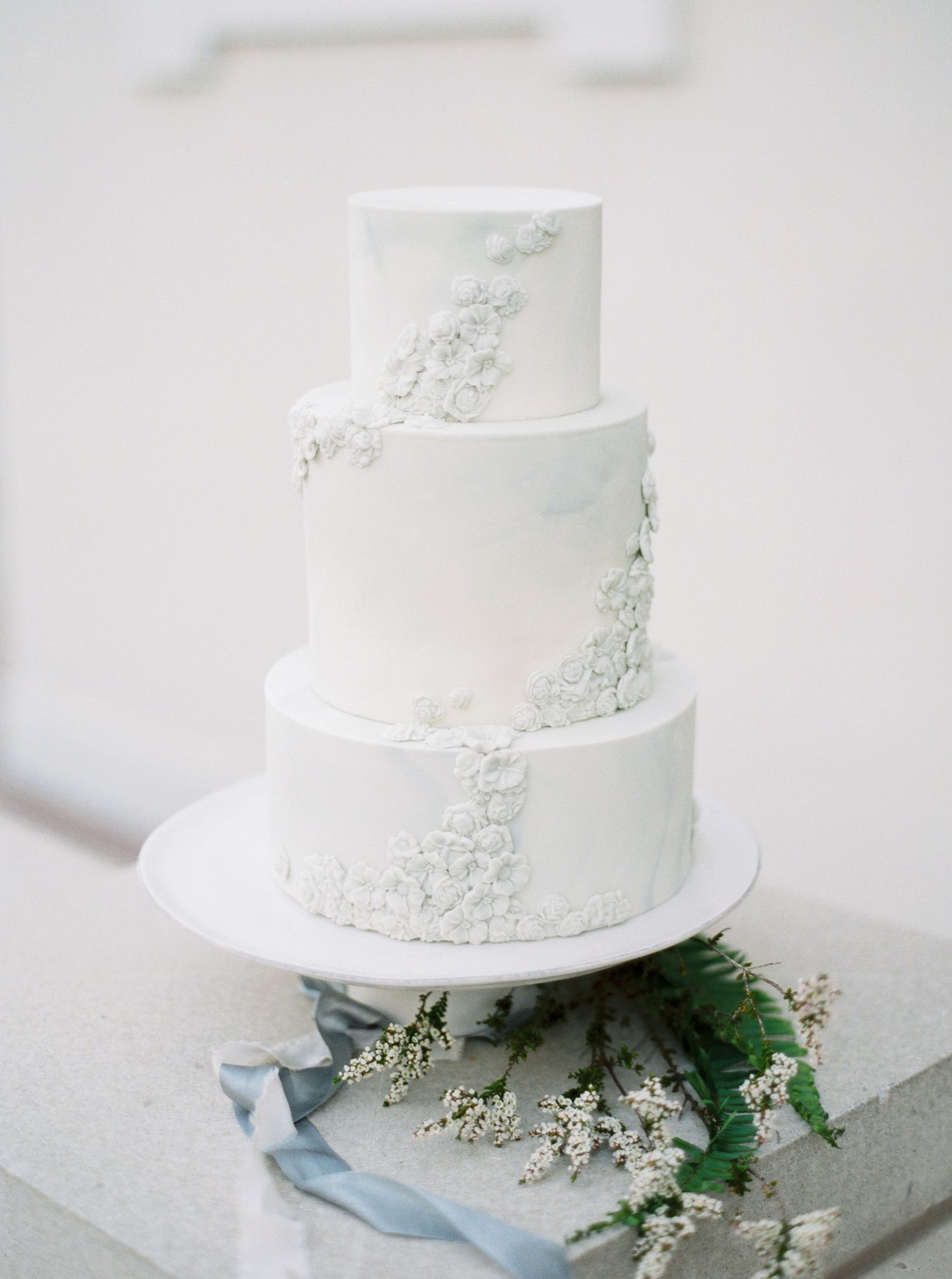 A series of elegant white wedding cakes with delicate floral details arranged in a minimalist style against a light background.