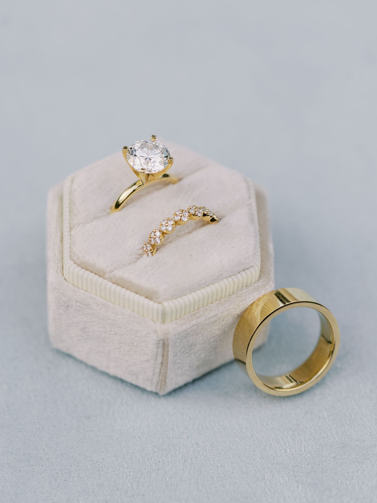 Gold engagement rings displayed on cream-colored velvet ring boxes against a gray background.