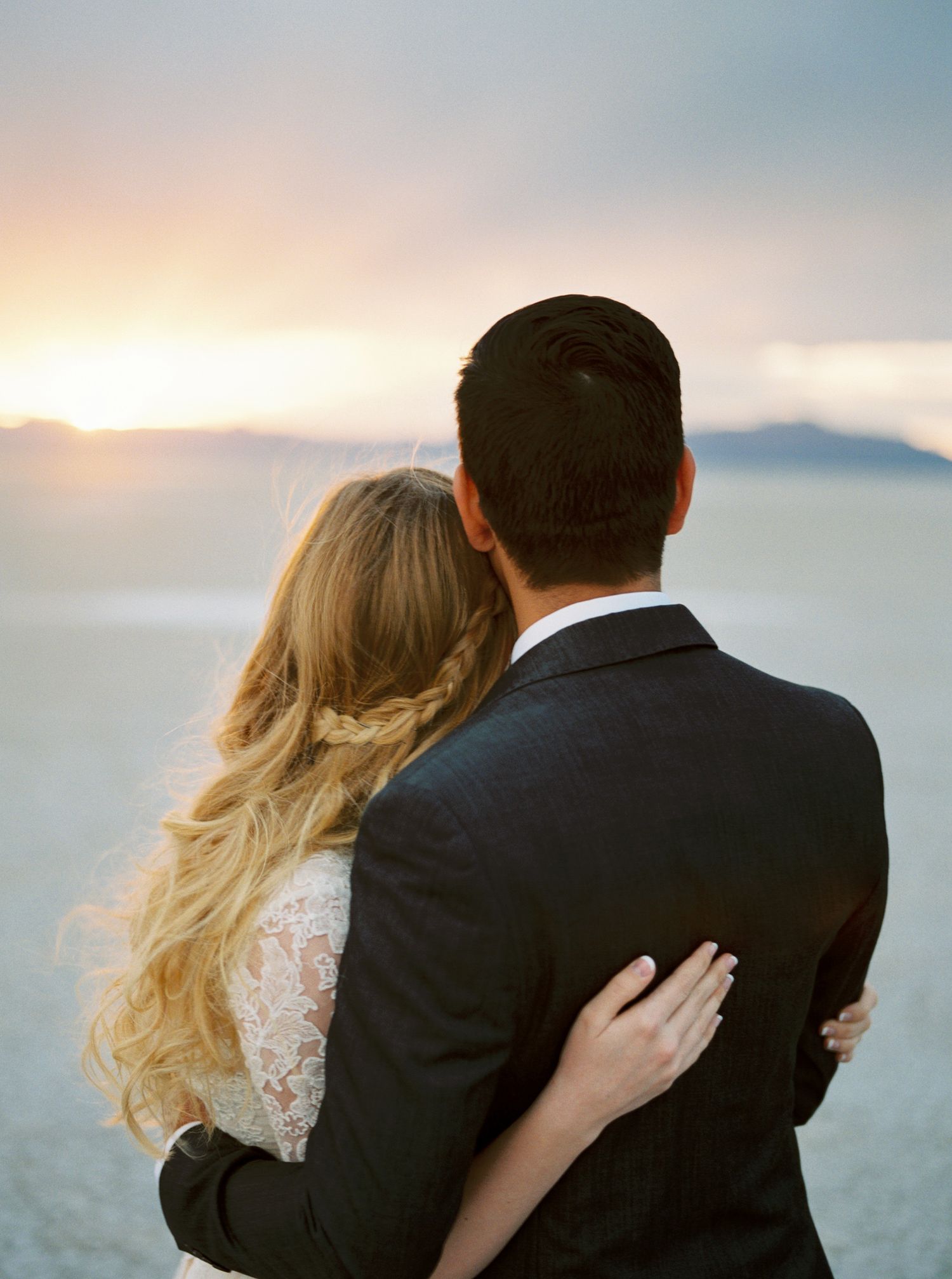 A couple embraces while watching a serene sunset over misty mountains, creating a romantic silhouette against the sky.