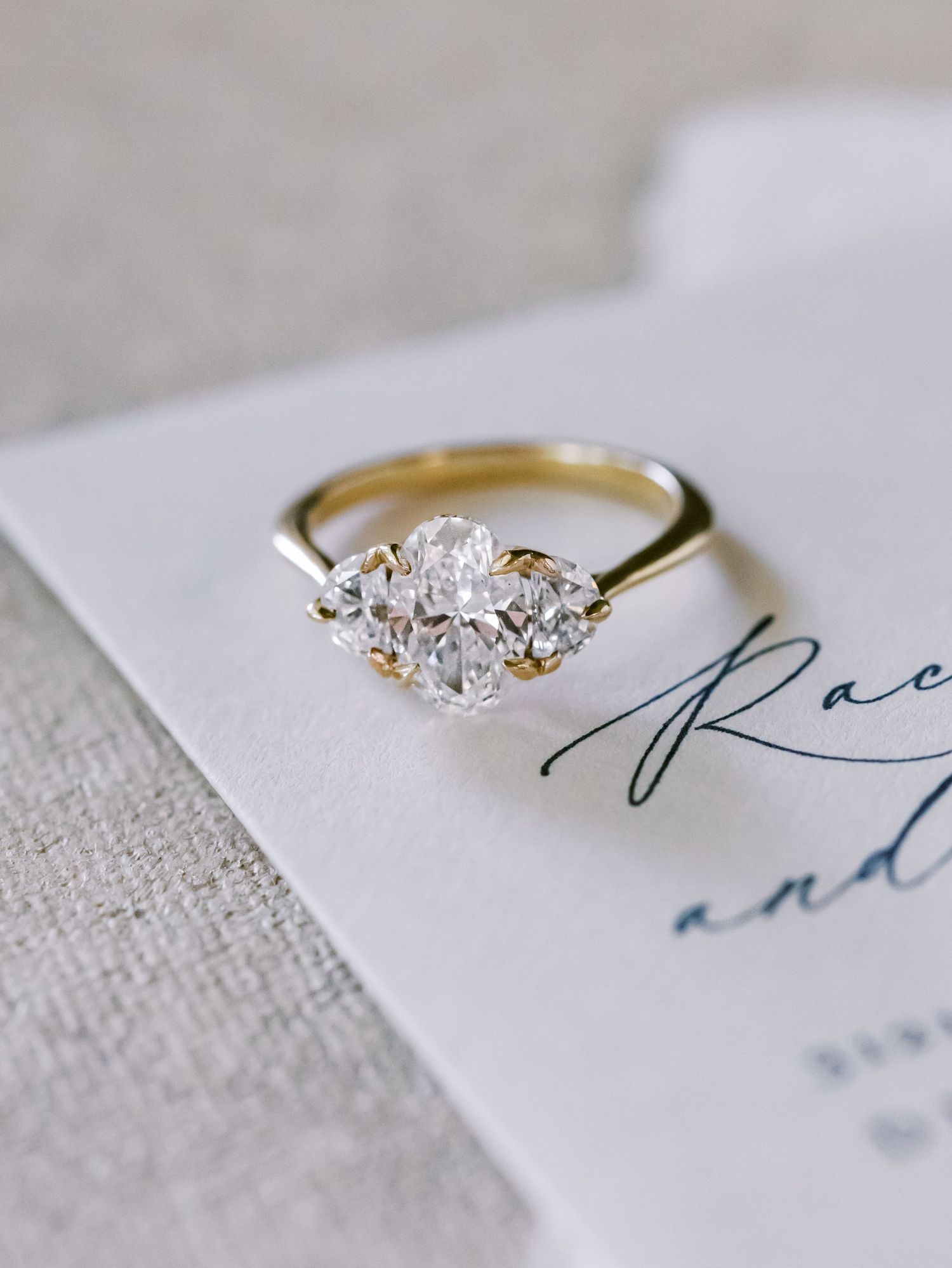 Gold engagement ring with oval diamond cluster on wedding invitation card.