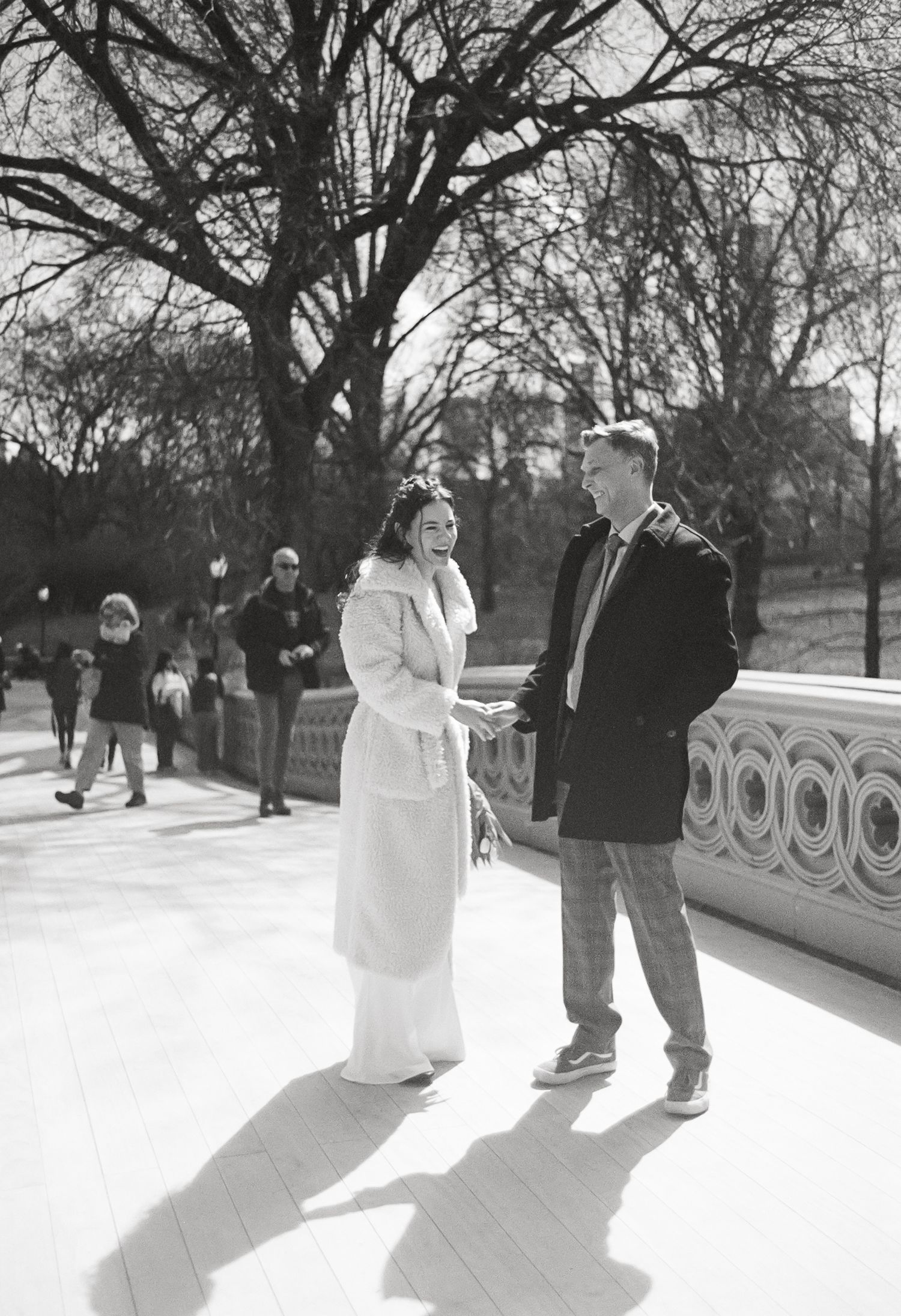 Black and white photo of a couple standing on Bow Bridge in Central Park, NYC, on a winter day.