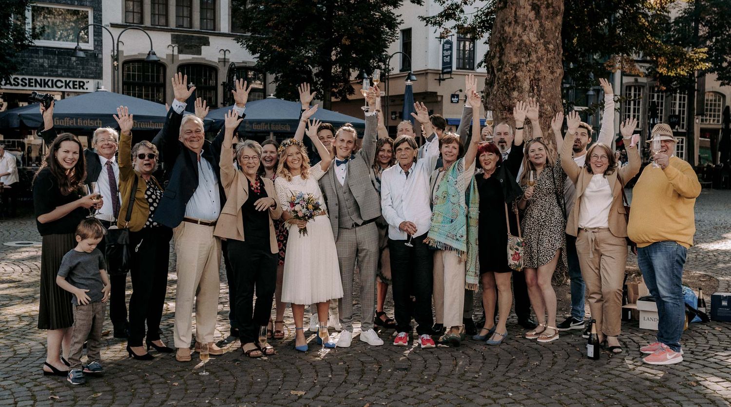 Wedding party and guests celebrating on a city street with raised arms.