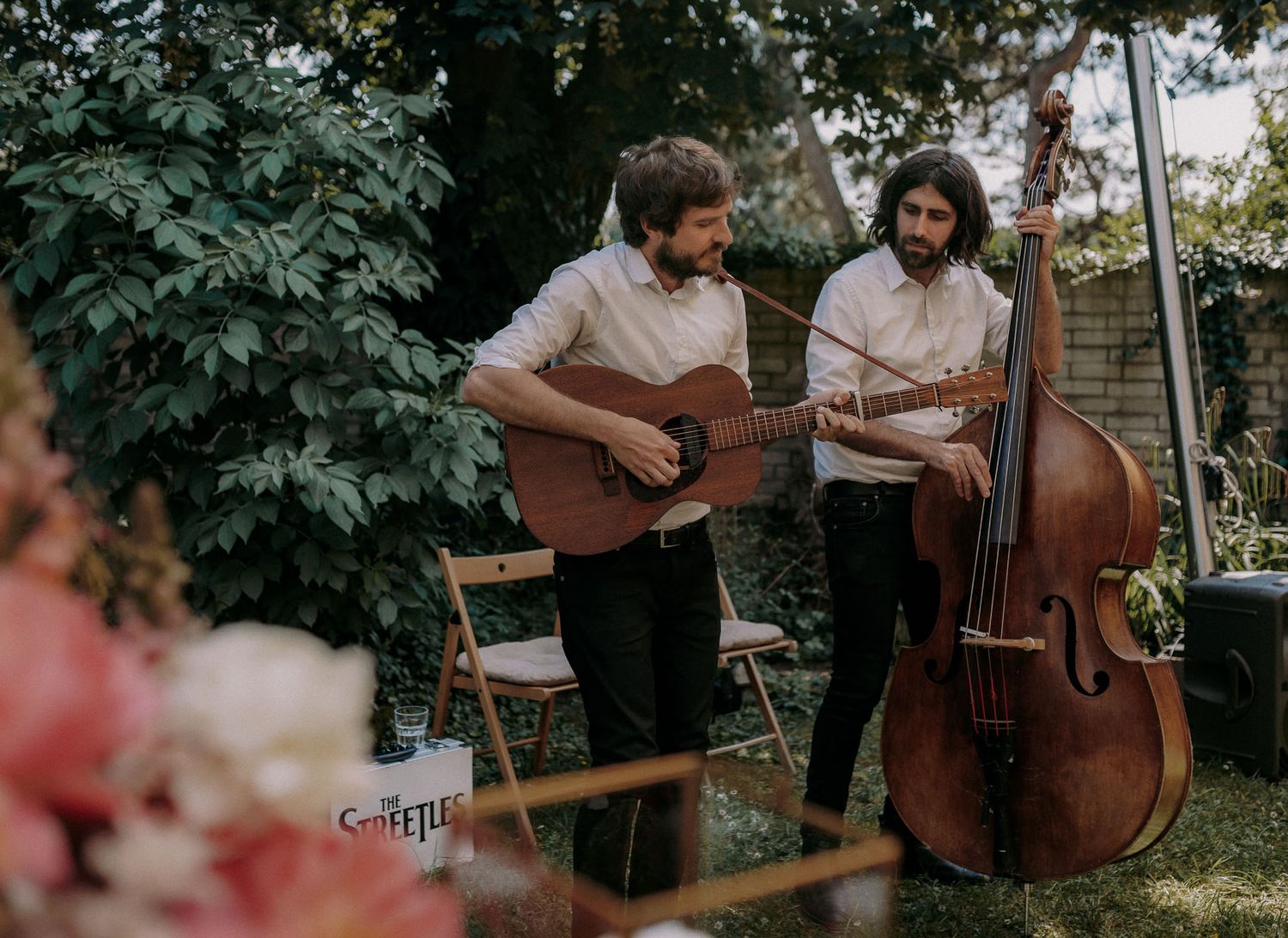 Musicians perform with acoustic guitar and upright bass in a garden setting.