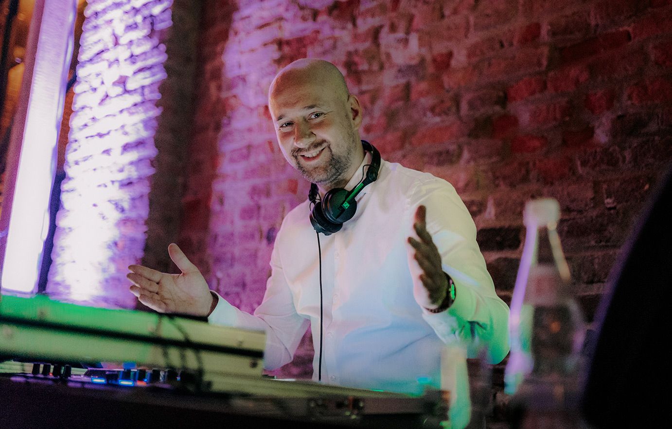 DJ performs at turntables with pink-lit brick wall backdrop.