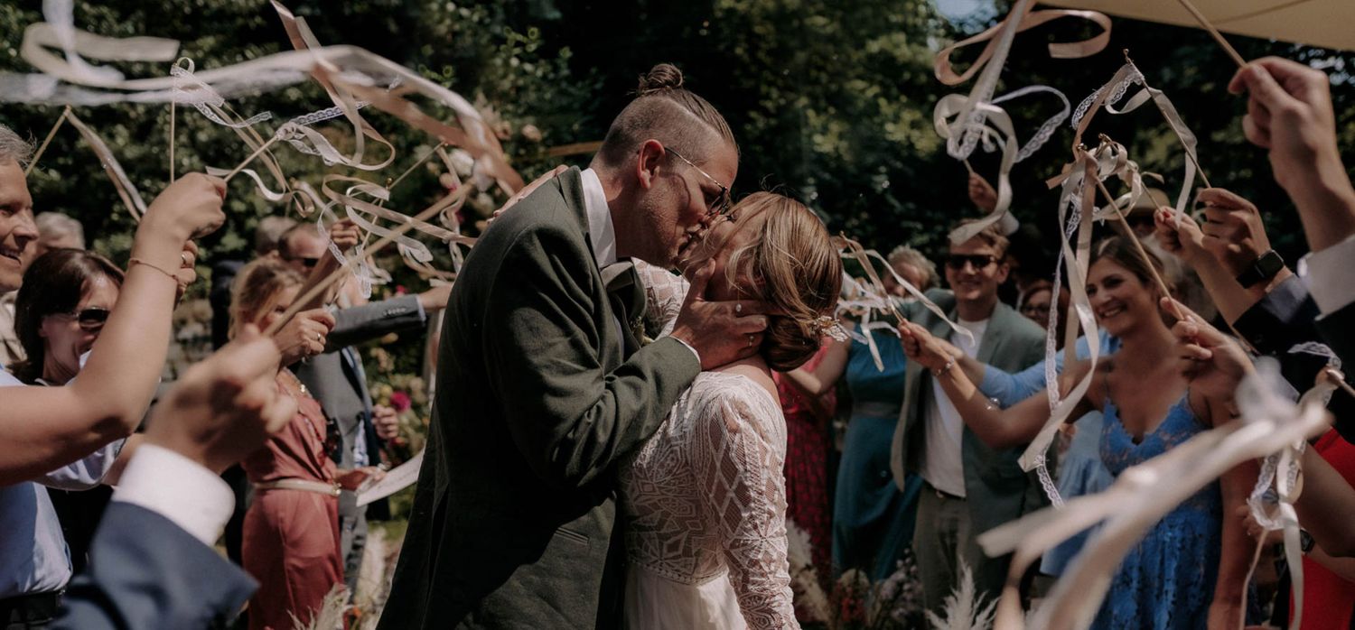 Newlyweds share an intimate moment under waving ribbons during an outdoor ceremony.