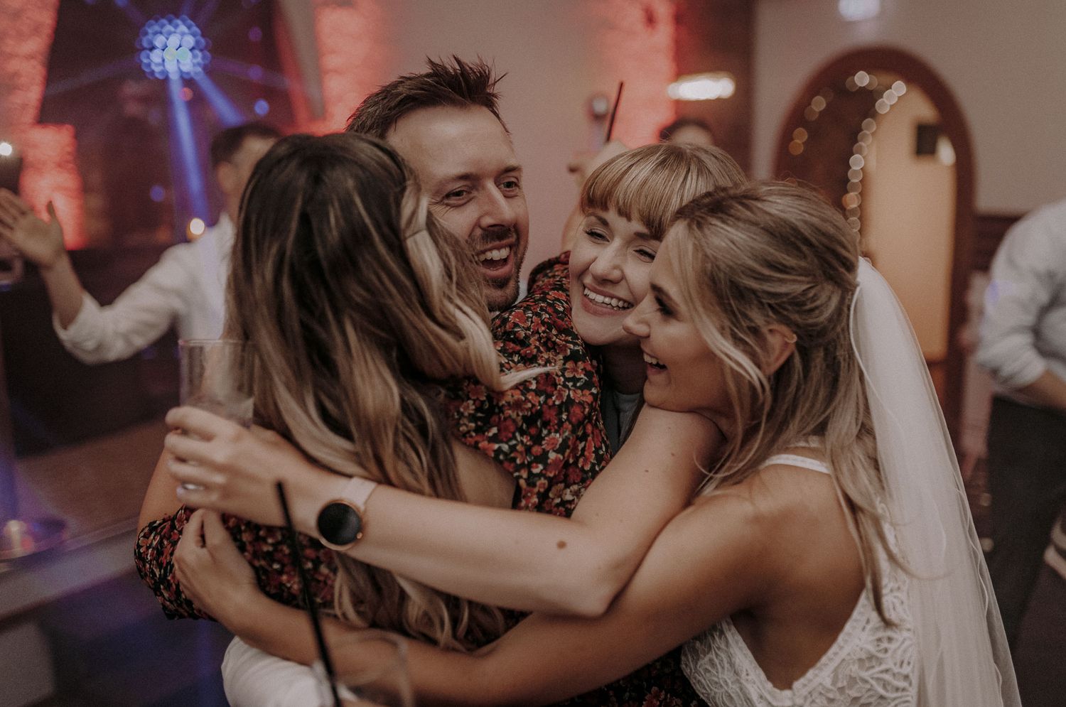 Wedding guests dancing and embracing joyfully on an illuminated dance floor.