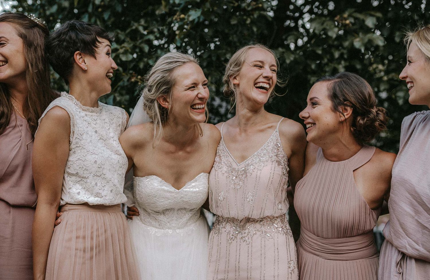 Bridesmaids in blush dresses share a candid laughing moment together.