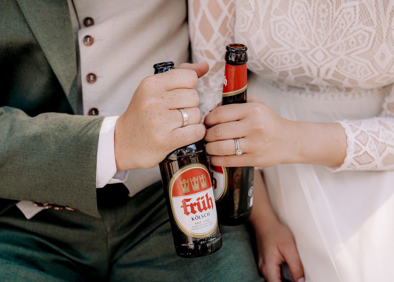 Close-up of newlyweds' hands clinking beer bottles together showing wedding rings.