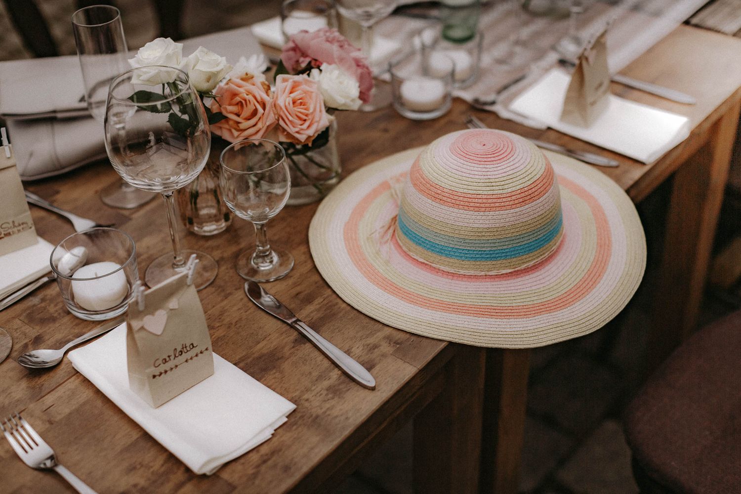 An elegant place setting with a striped sun hat and peach roses on a wooden table.