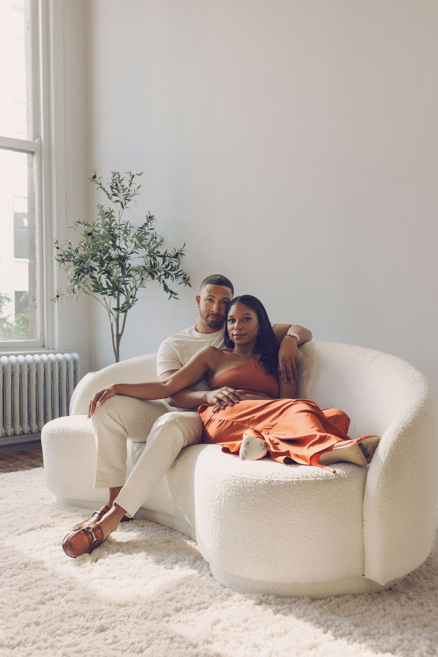 Couple relaxing together on a plush white curved sofa in a bright, minimalist room with white carpet.