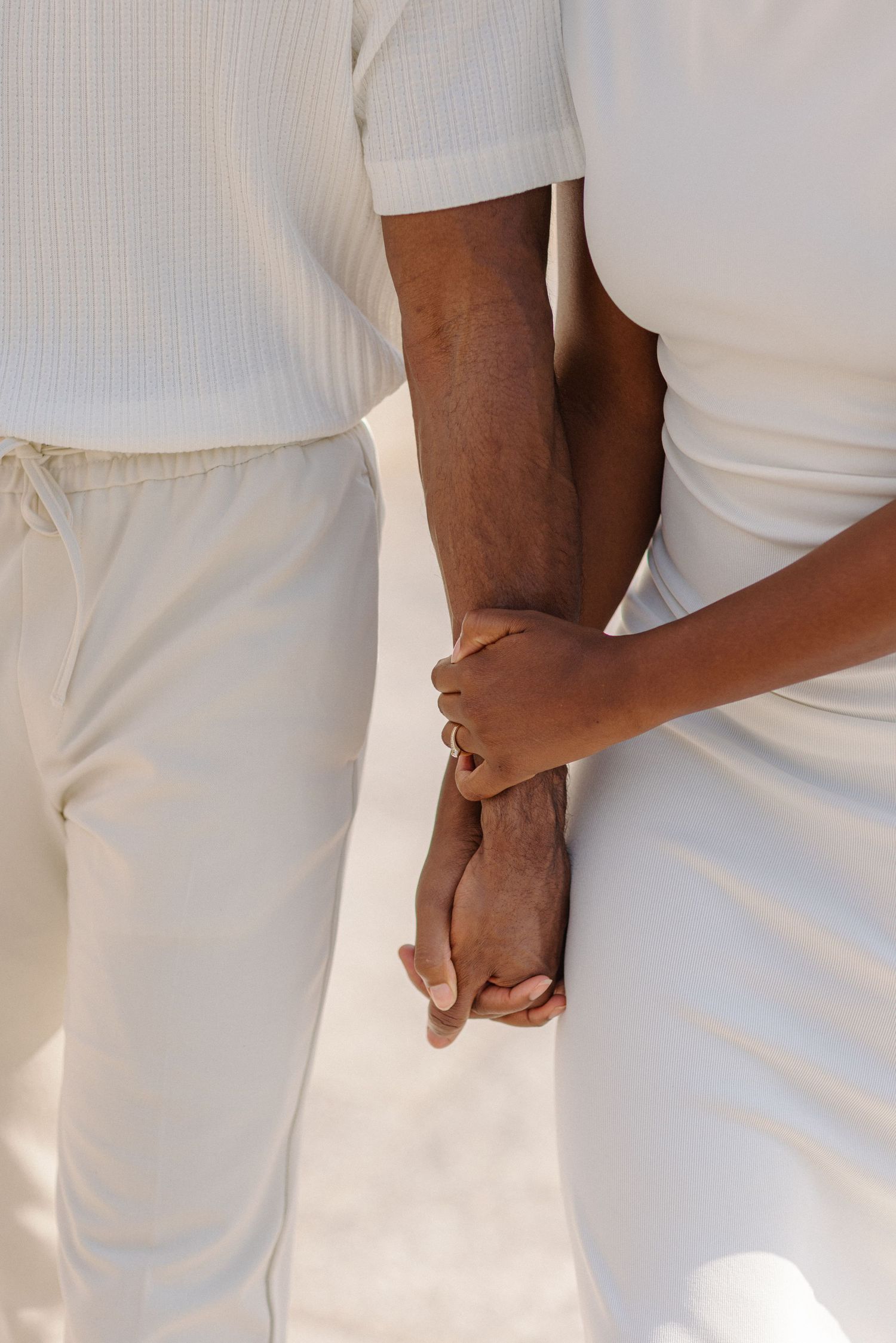Close-up of two people holding hands while wearing matching white outfits.