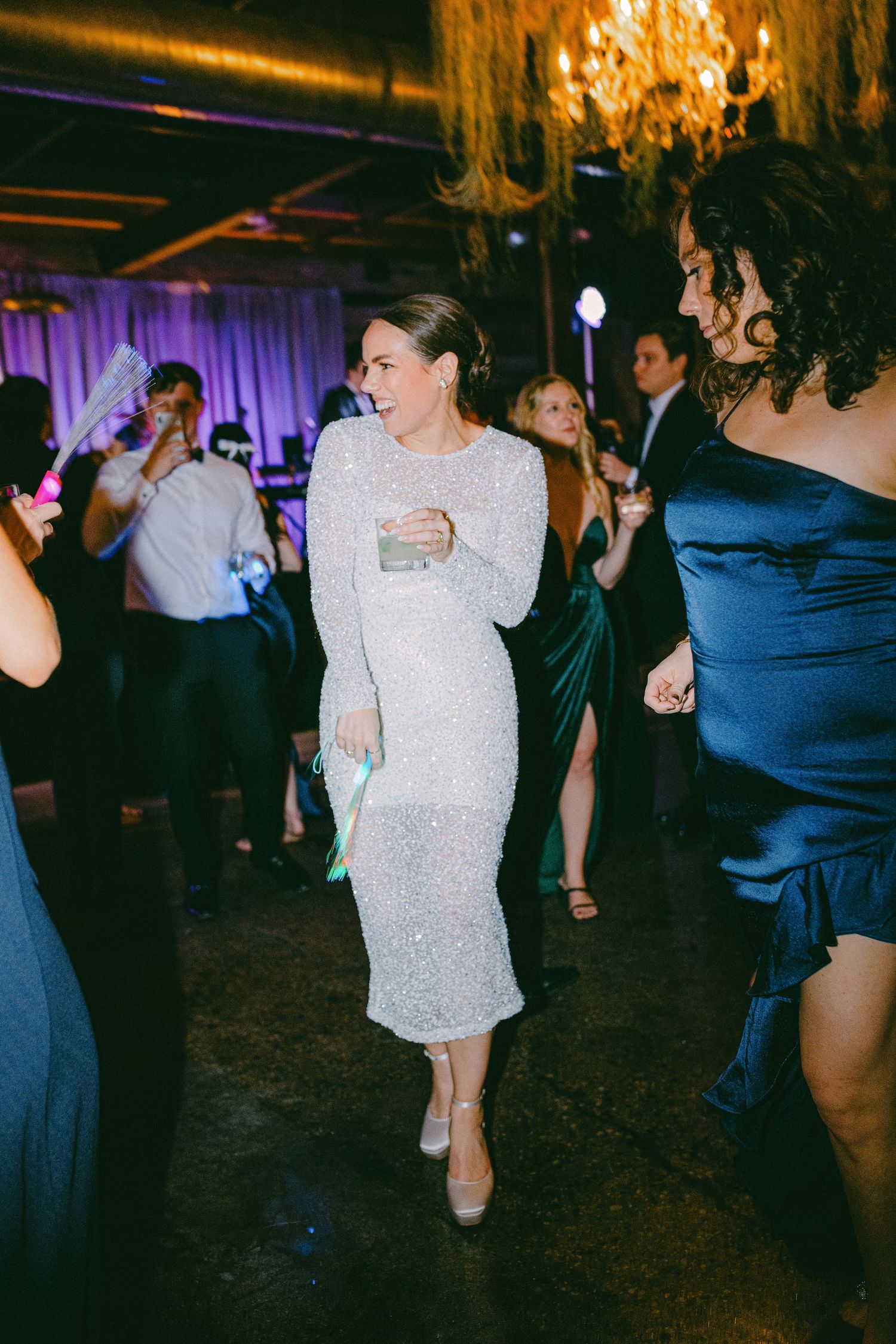 A person in a sparkly white dress dances at an elegant reception with party guests.