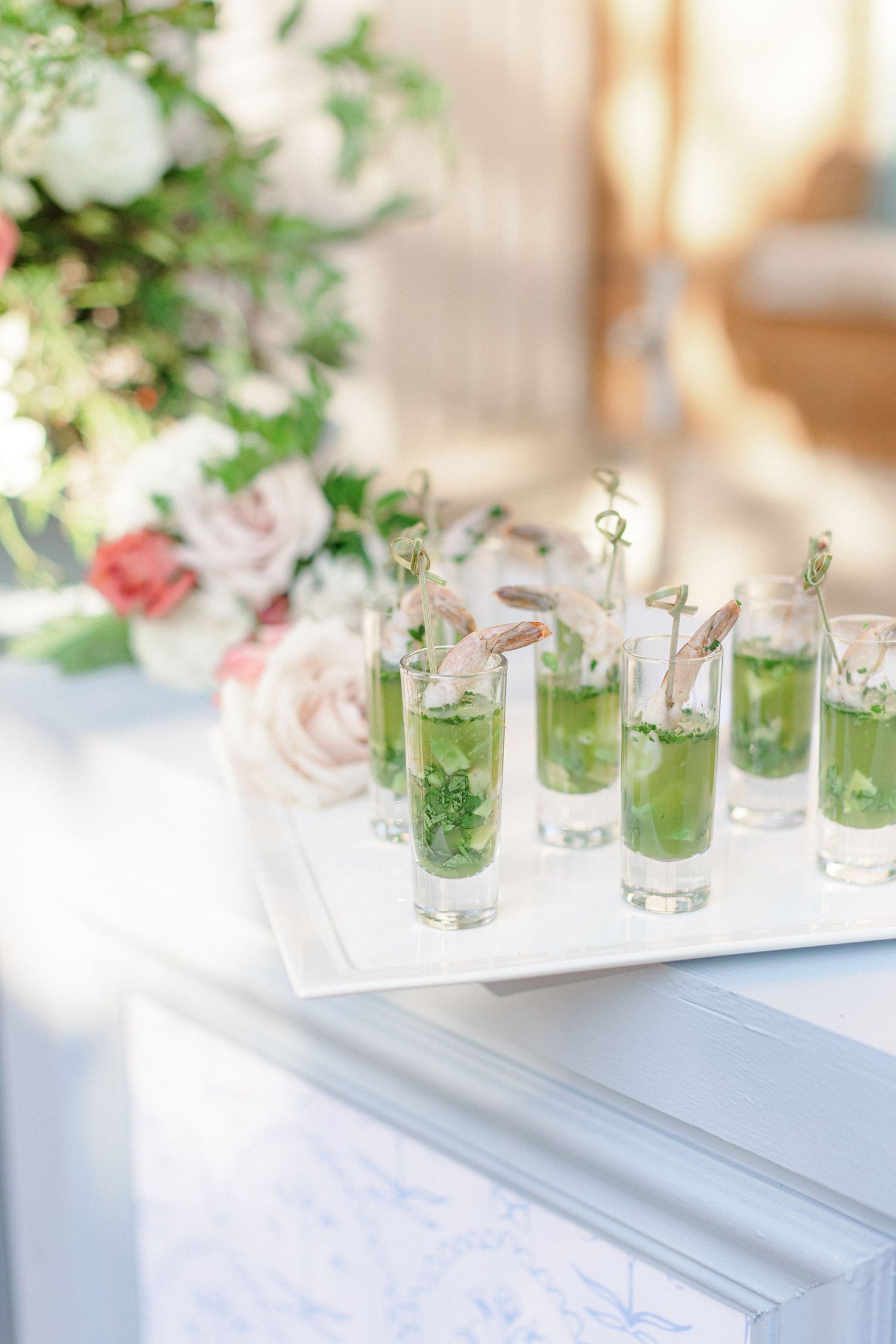 Green cocktails garnished with flowers lined up on white tray at wedding reception.