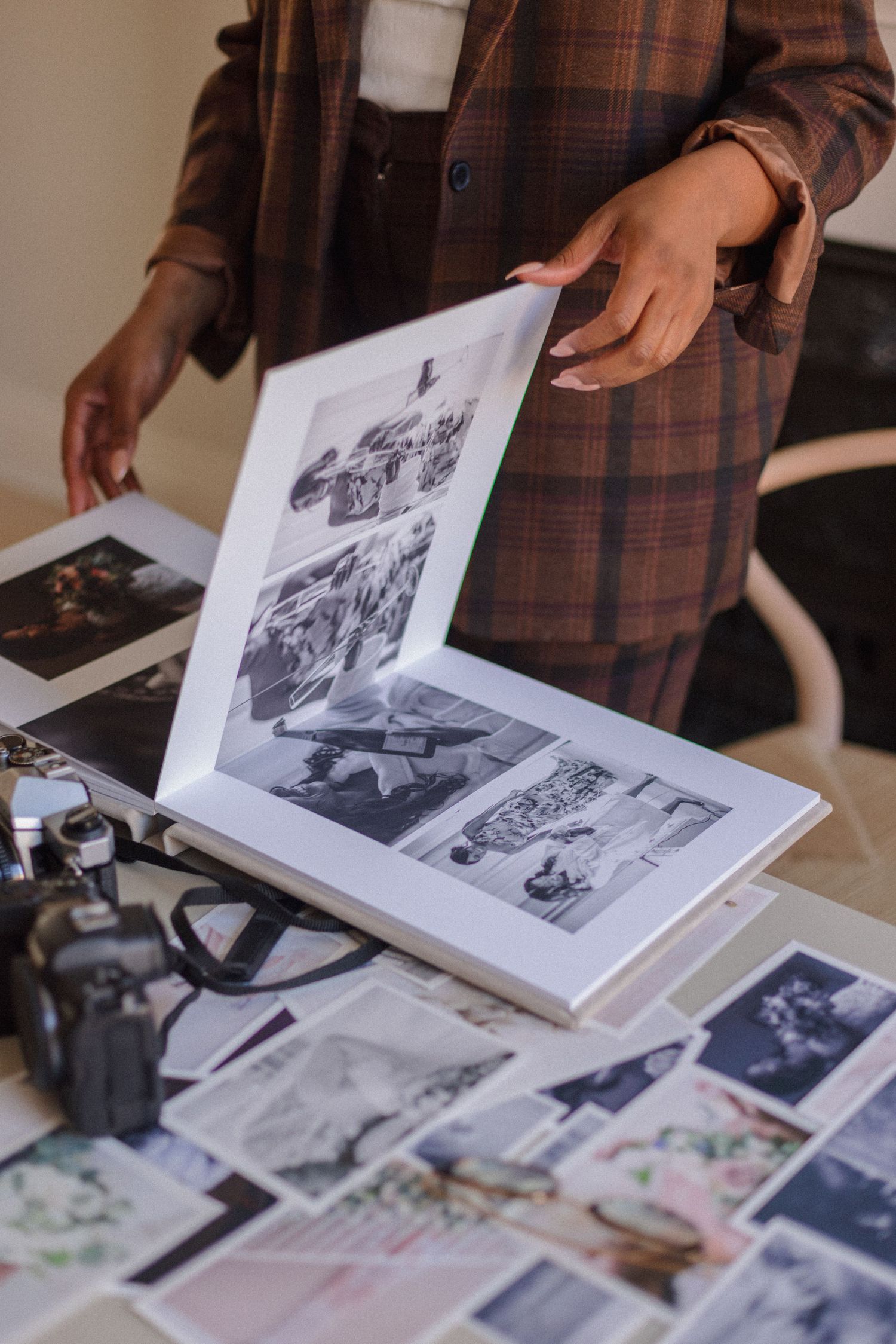 Photography book being reviewed with vintage camera and scattered photographs on a wooden surface.