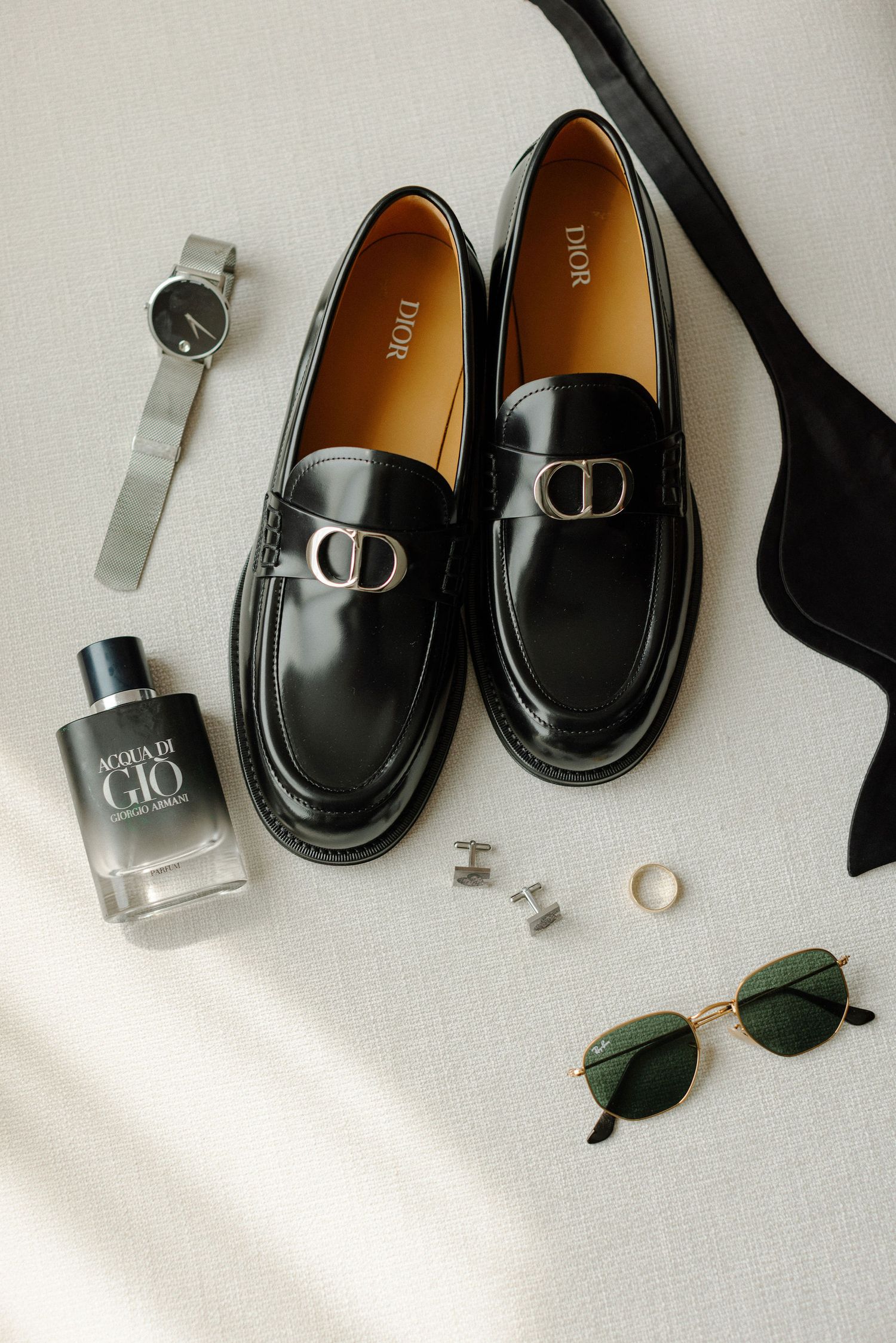 Black leather loafers with accessories including cologne, watch, and sunglasses on white surface.