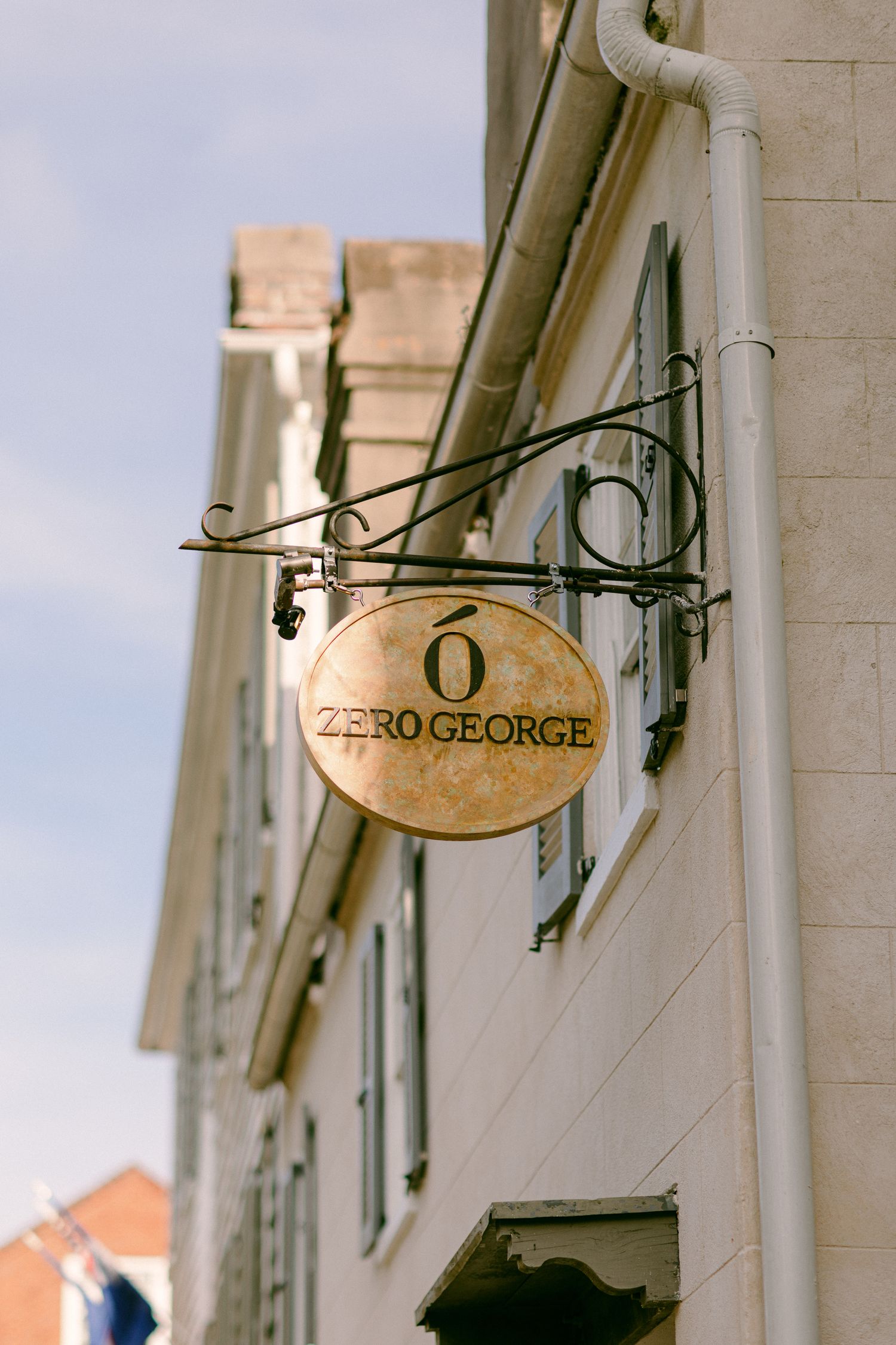 Vintage metal shop sign mounted on a white stone building wall in a European style street setting.