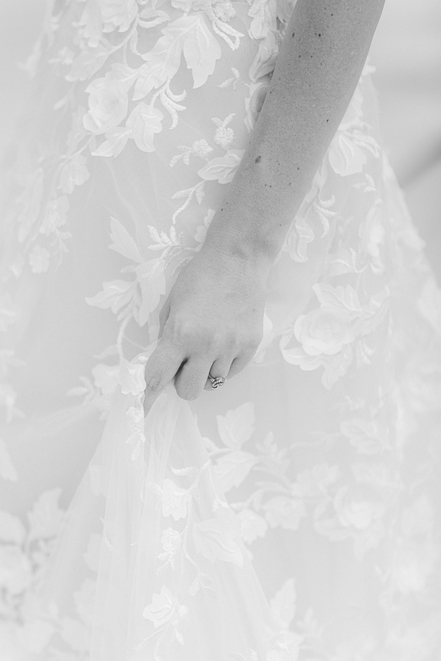 Close-up detail of delicate lace pattern on white wedding dress fabric with ring.