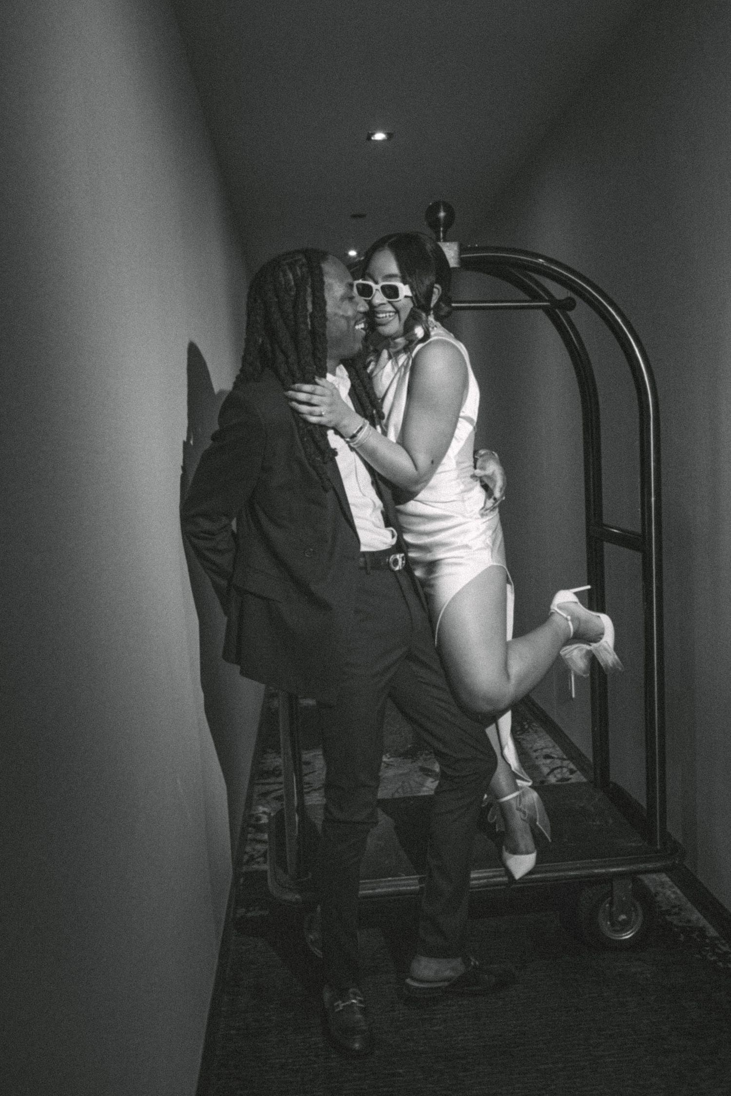 Romantic black and white photo with luggage cart in hotel hallway.