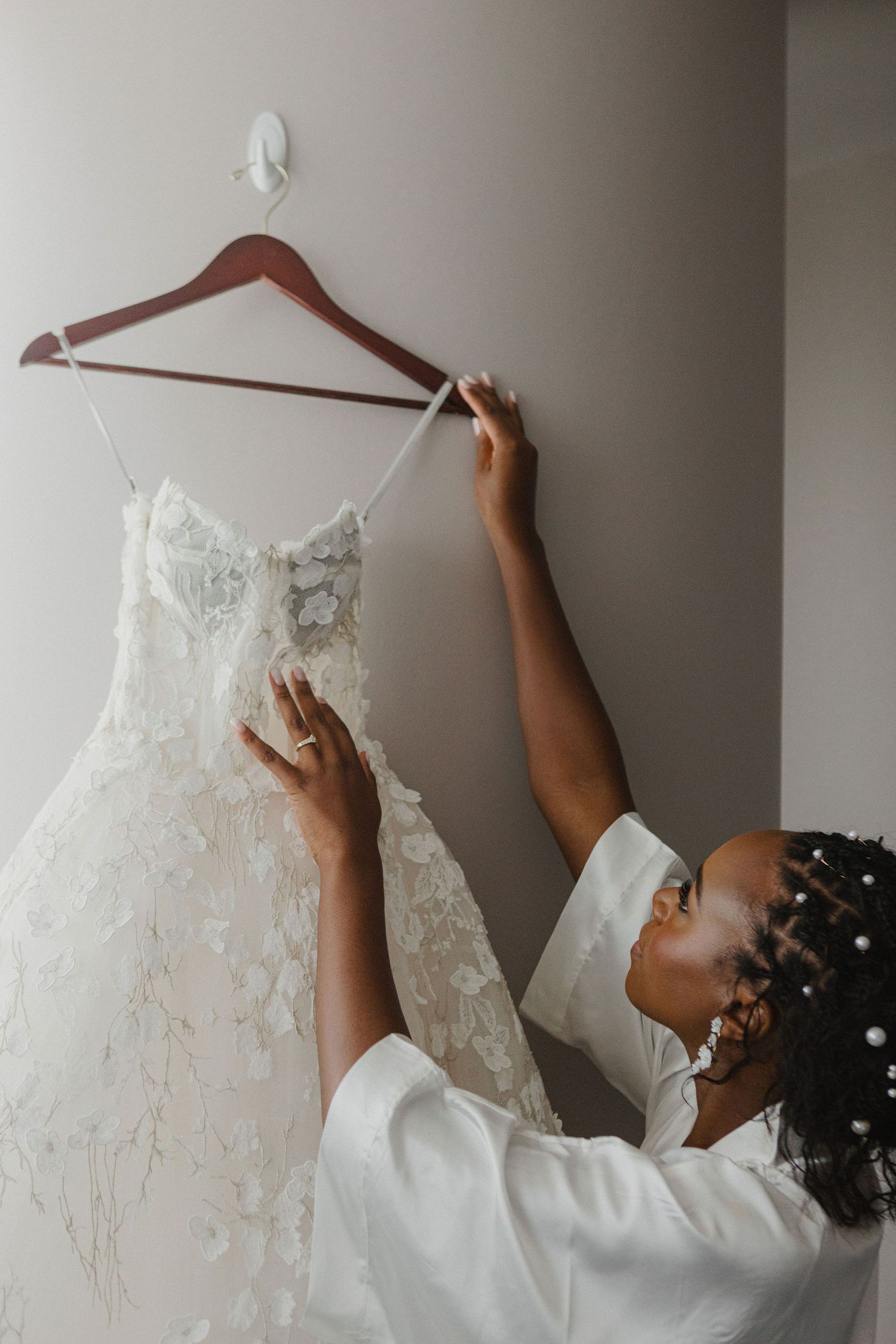 Wedding dress with intricate lace details hanging on a wooden hanger.