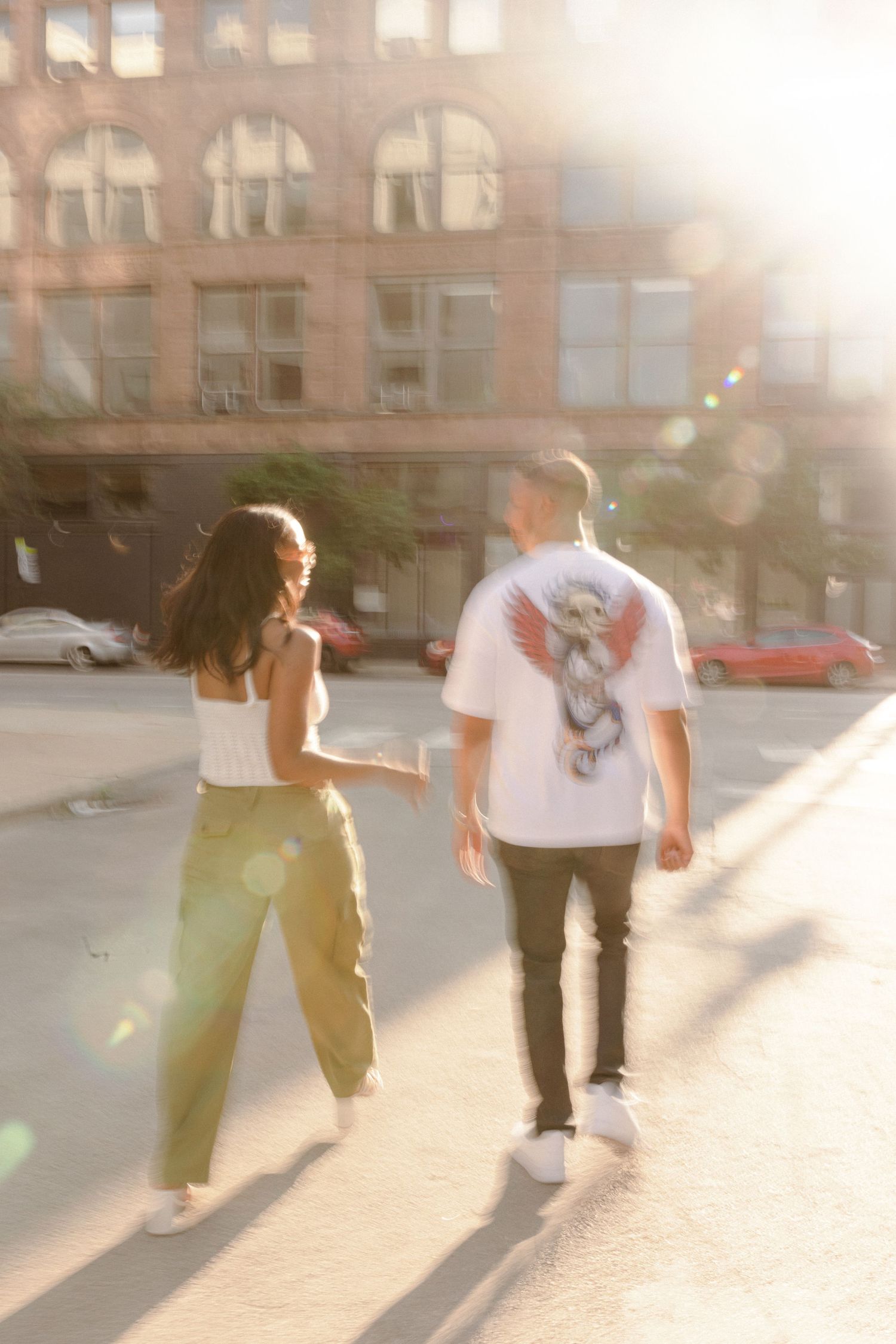 Couple strolling in sunlit city street with lens flare effect.