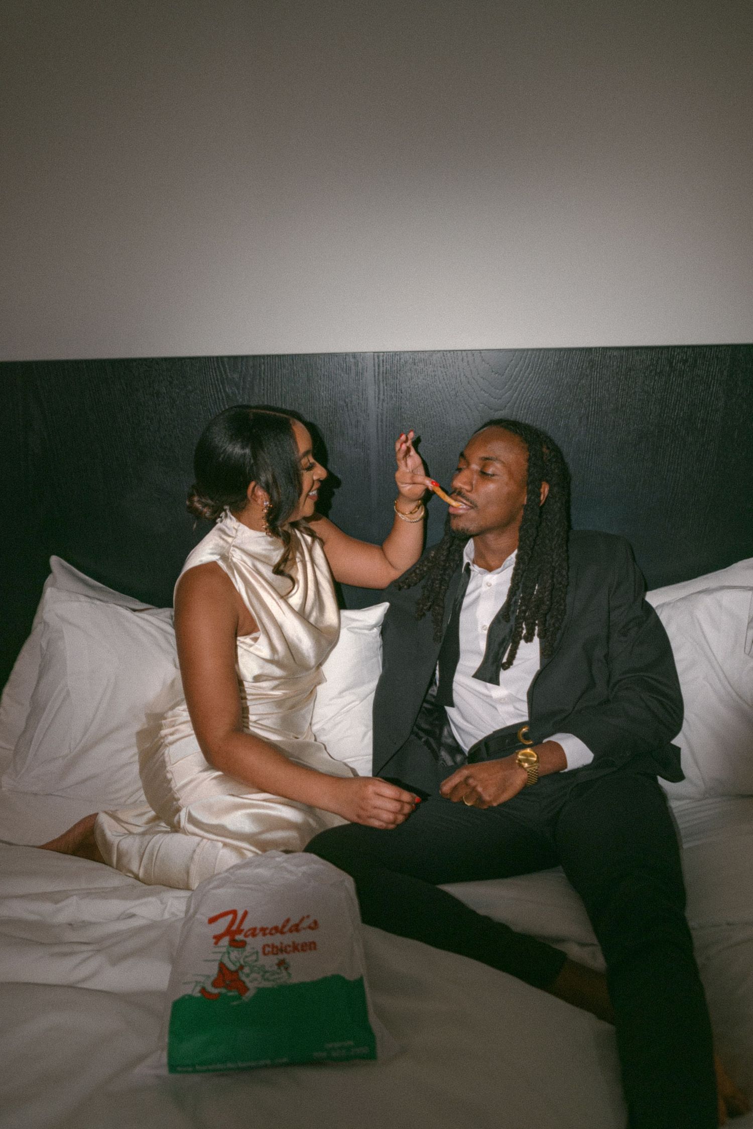 Playful couple in formal wear sharing intimate moment on bed.