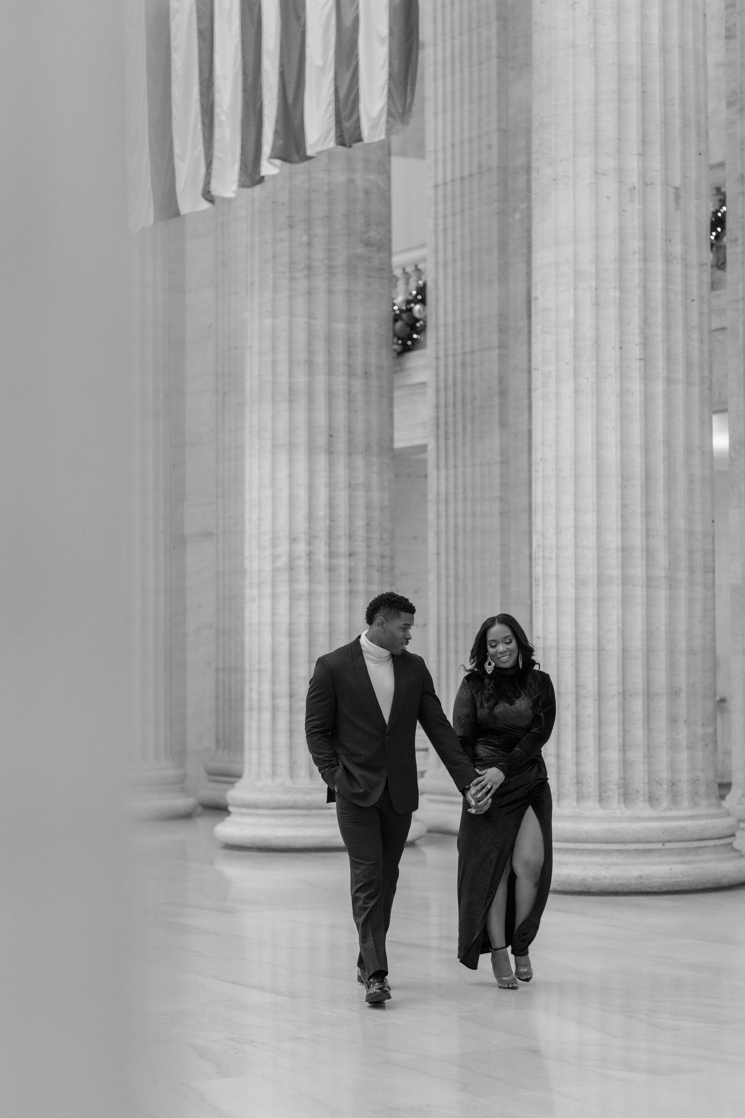 Elegant couple walking between classical columns in black and white photograph.