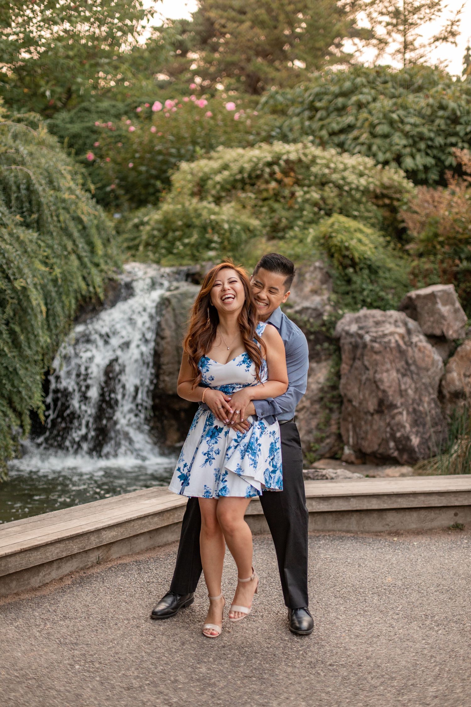 Romantic couple embracing by waterfall in formal attire and blue floral dress.