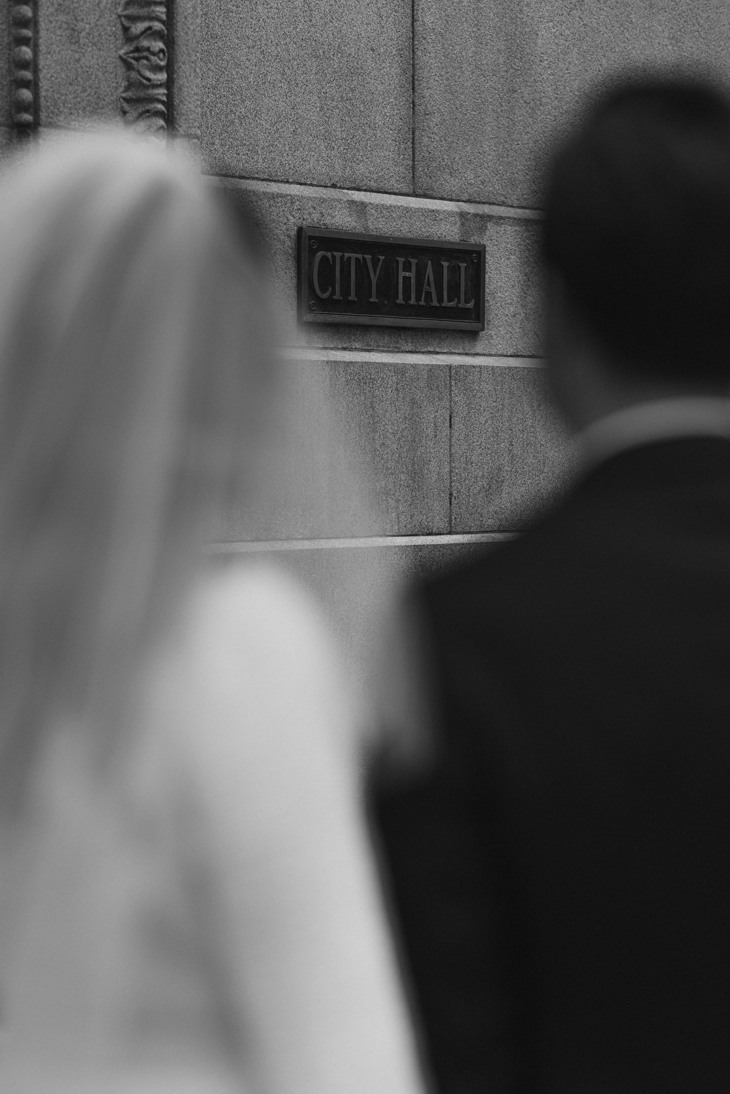 Black and white photo showing City Hall sign with wedding couple in soft focus.