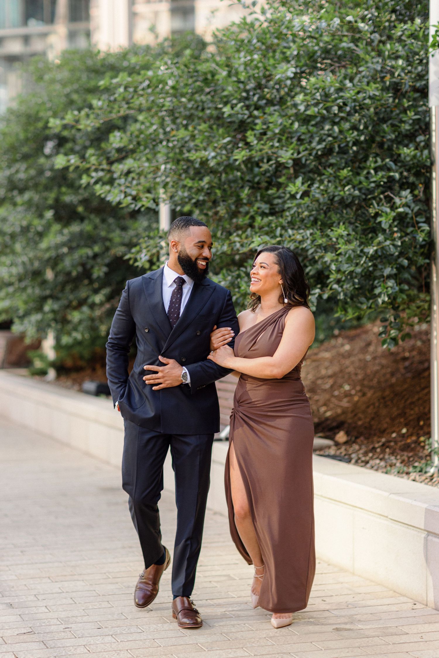 Couple walking together on brick path wearing brown gown and navy suit.