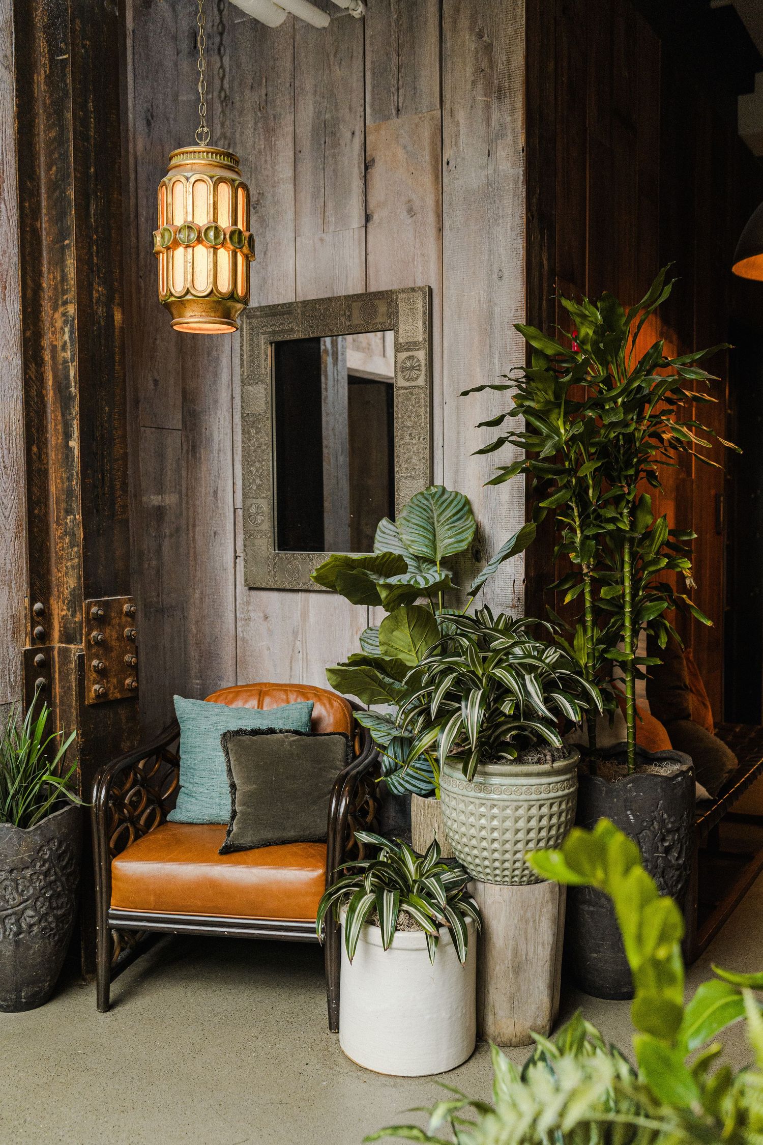Modern lounge corner featuring leather chair, hanging pendant light, and lush potted plants against wooden walls.