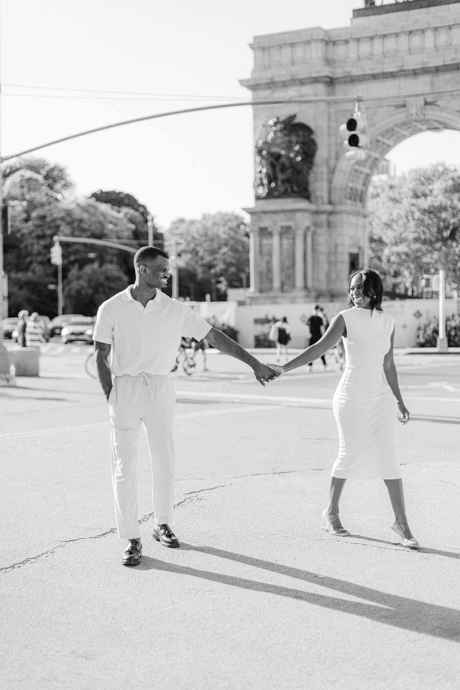 A black and white photo of a couple dancing near a monumental arch.