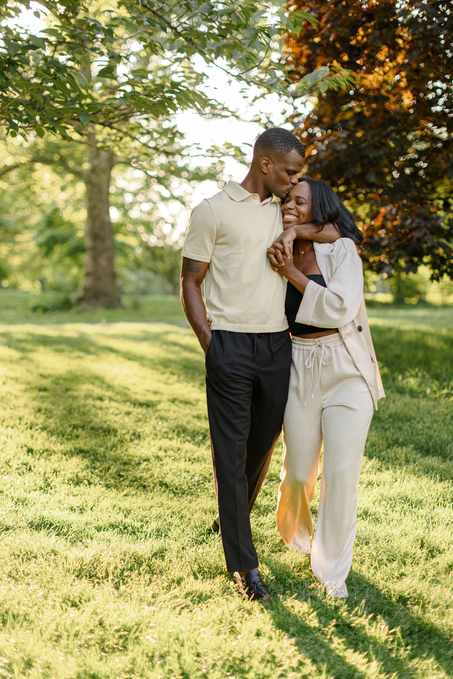 A couple sharing an intimate moment while standing in a sun-lit park.