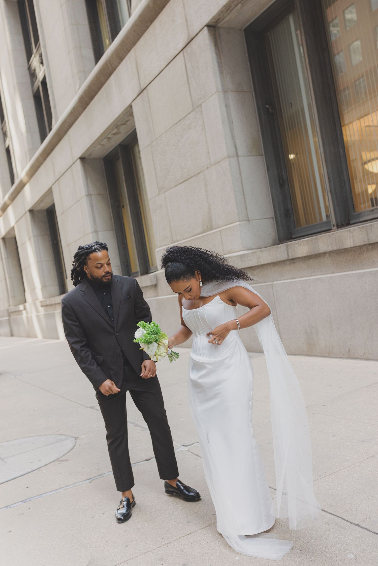 A playful wedding photo series showing a couple dancing and posing together in front of a white stone building.