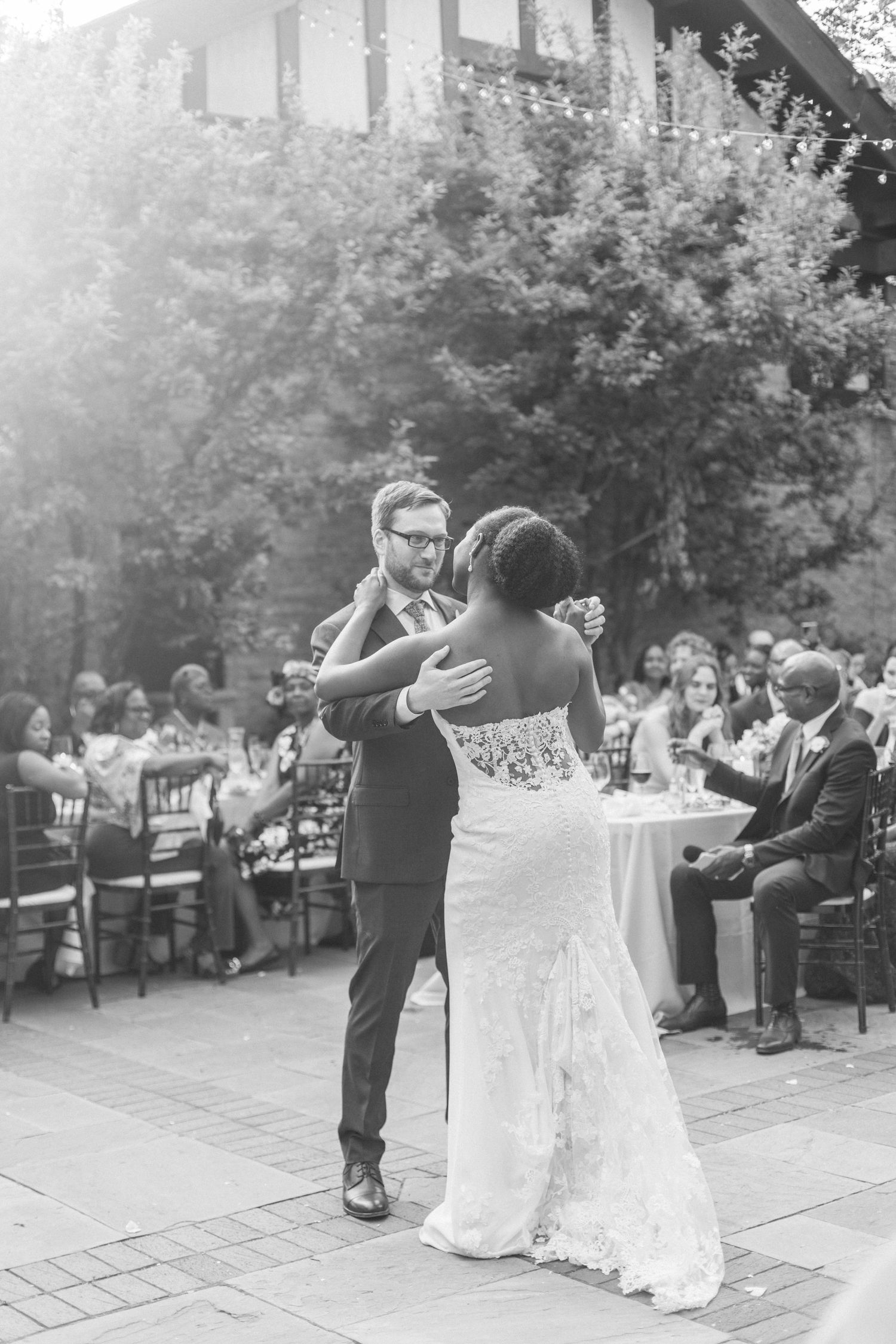 A couple shares their first dance at an outdoor wedding reception surrounded by guests.