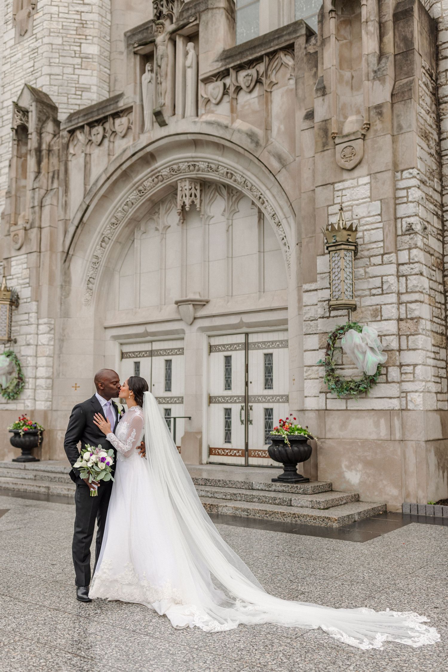 Wedding couple poses in front of a grand stone church entrance with gothic architecture.