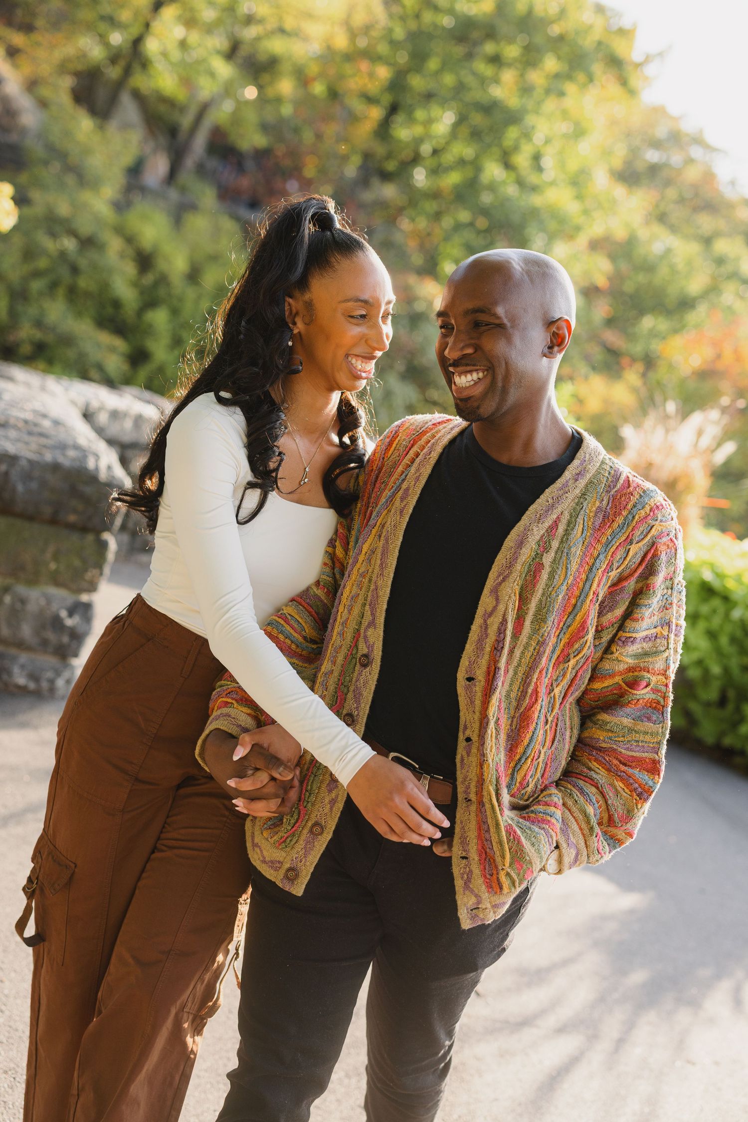 A couple shares joyful laughter while walking together outdoors on an autumn day.