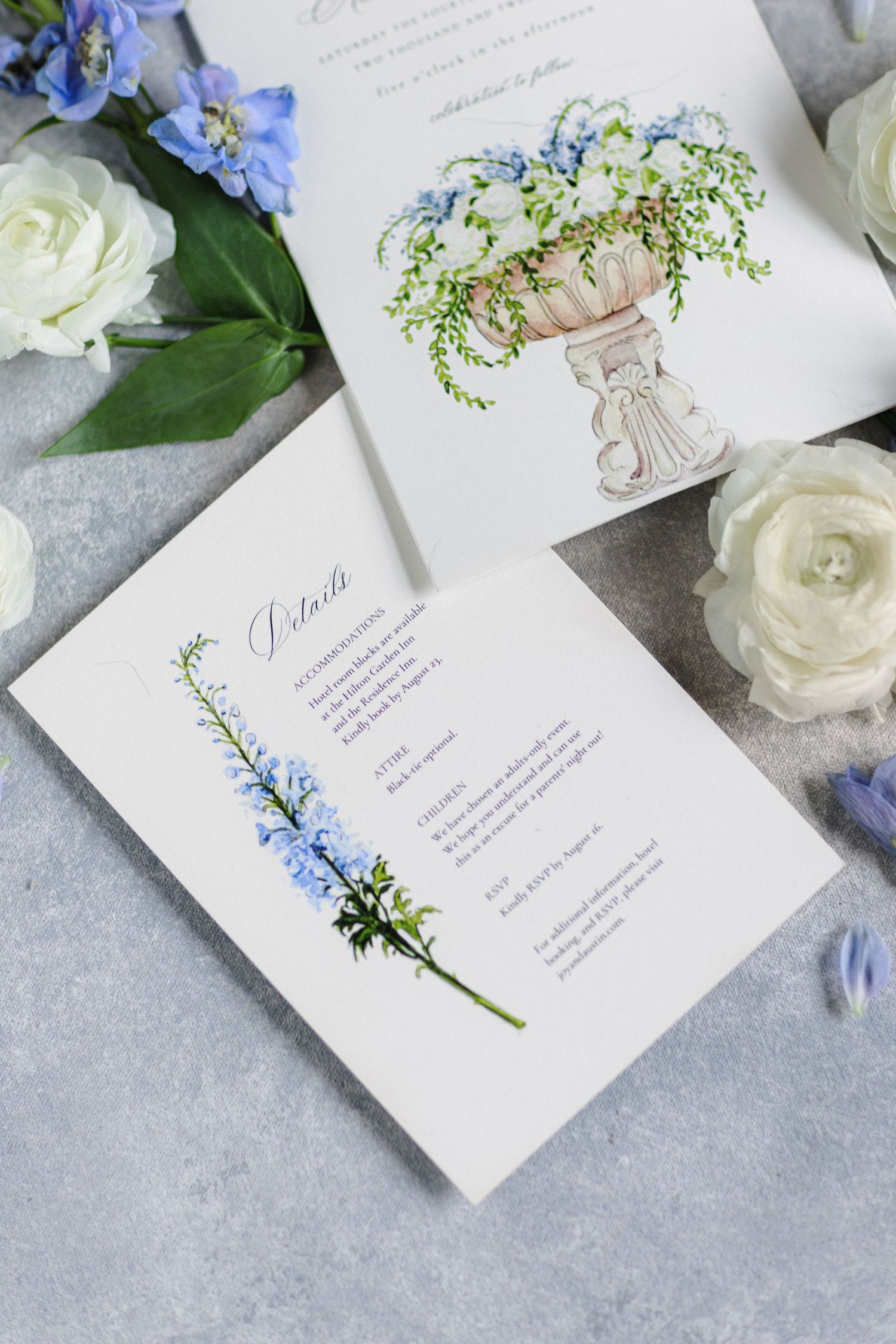 Elegant wedding invitation with delicate blue floral details and white roses displayed on a light gray marble background.