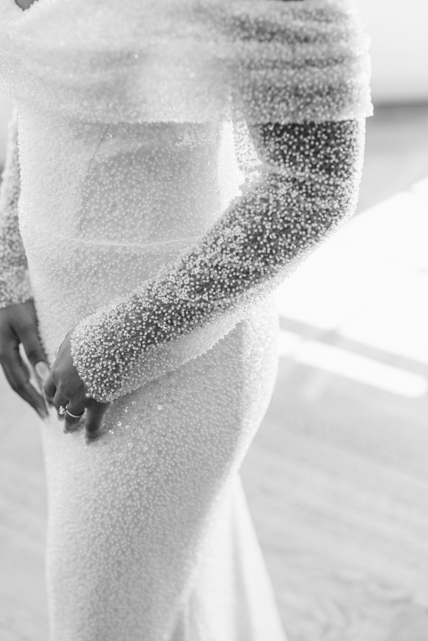 Black and white close-up of delicate lace sleeve detail and form-fitting bodice of an elegant wedding dress.